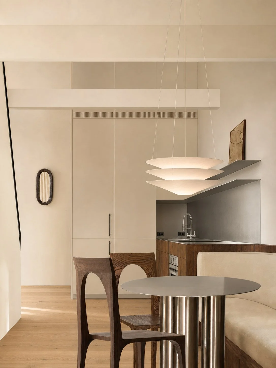 Kitchen and dining seen past a tiered pendant, with tall cream joinery and a stainless table