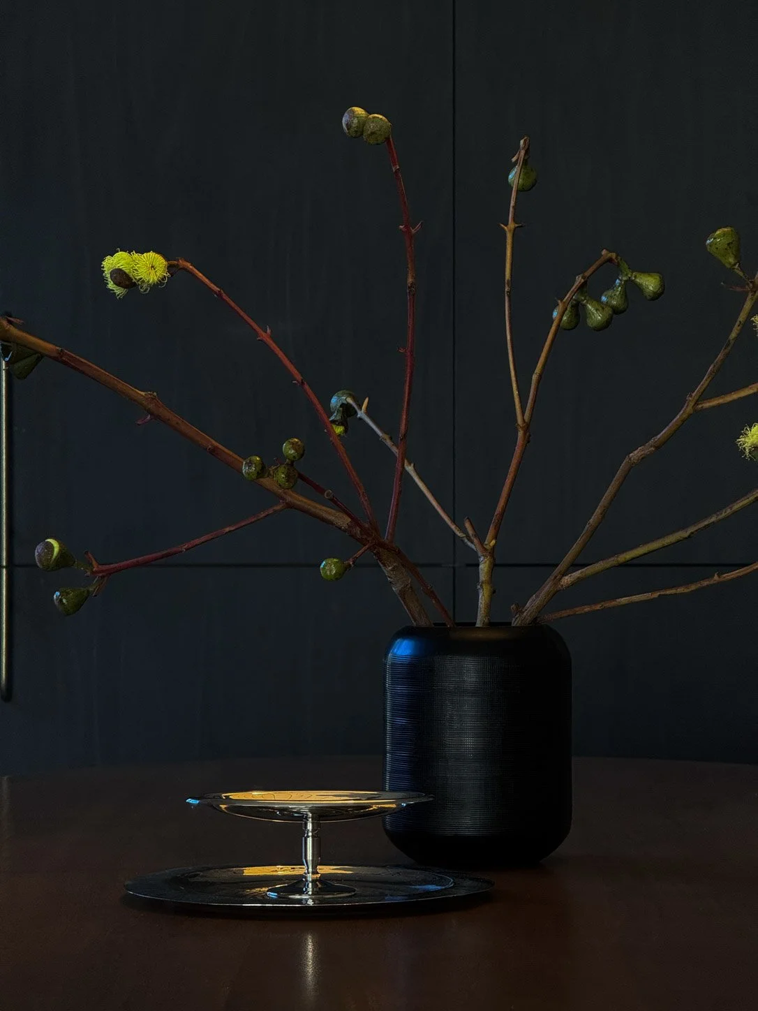 Gum blossom in a black vase with a silver comport, against charcoal joinery