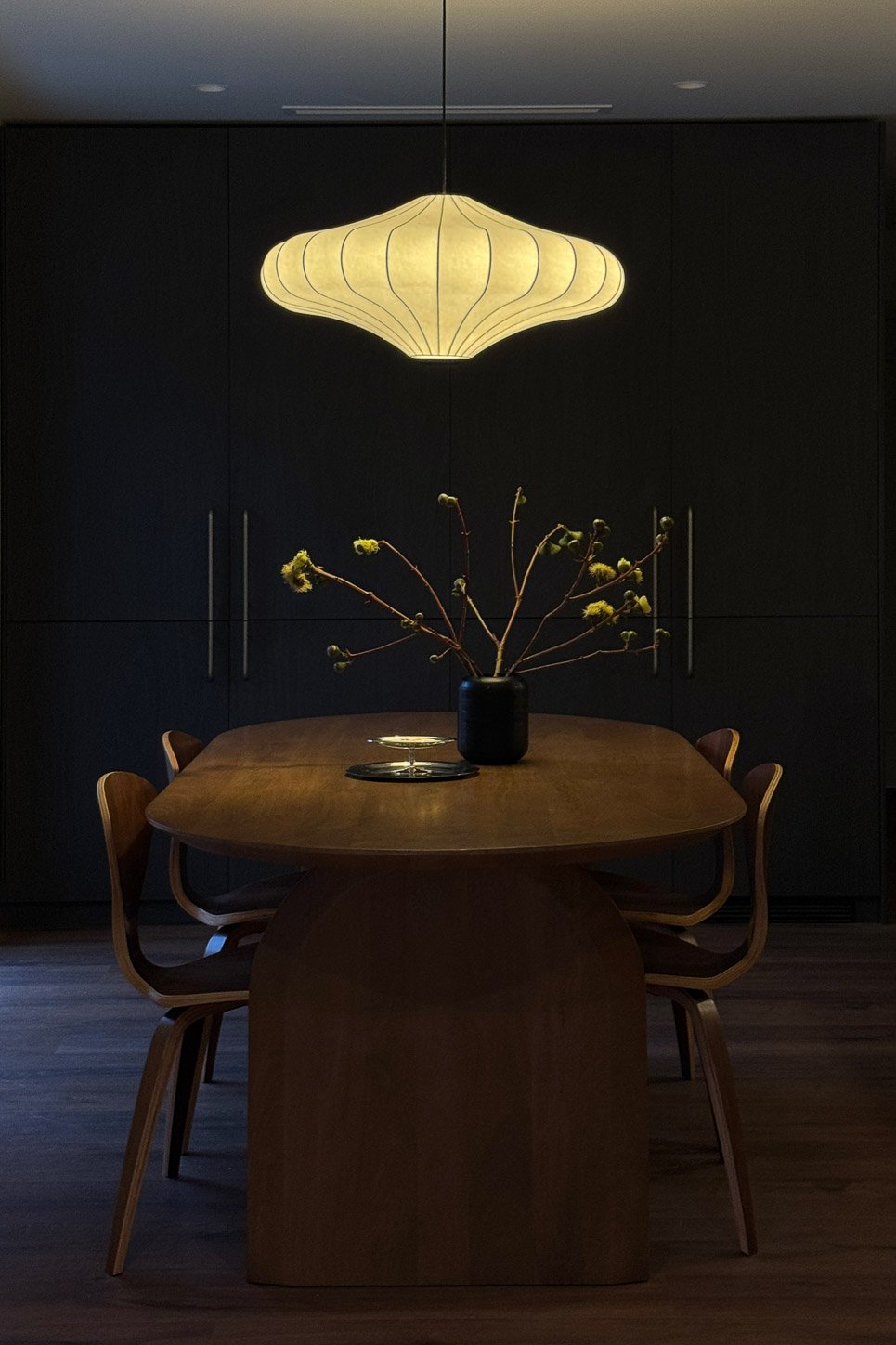 The dining room at night, saucer pendant lit above the walnut table and Cherner chairs