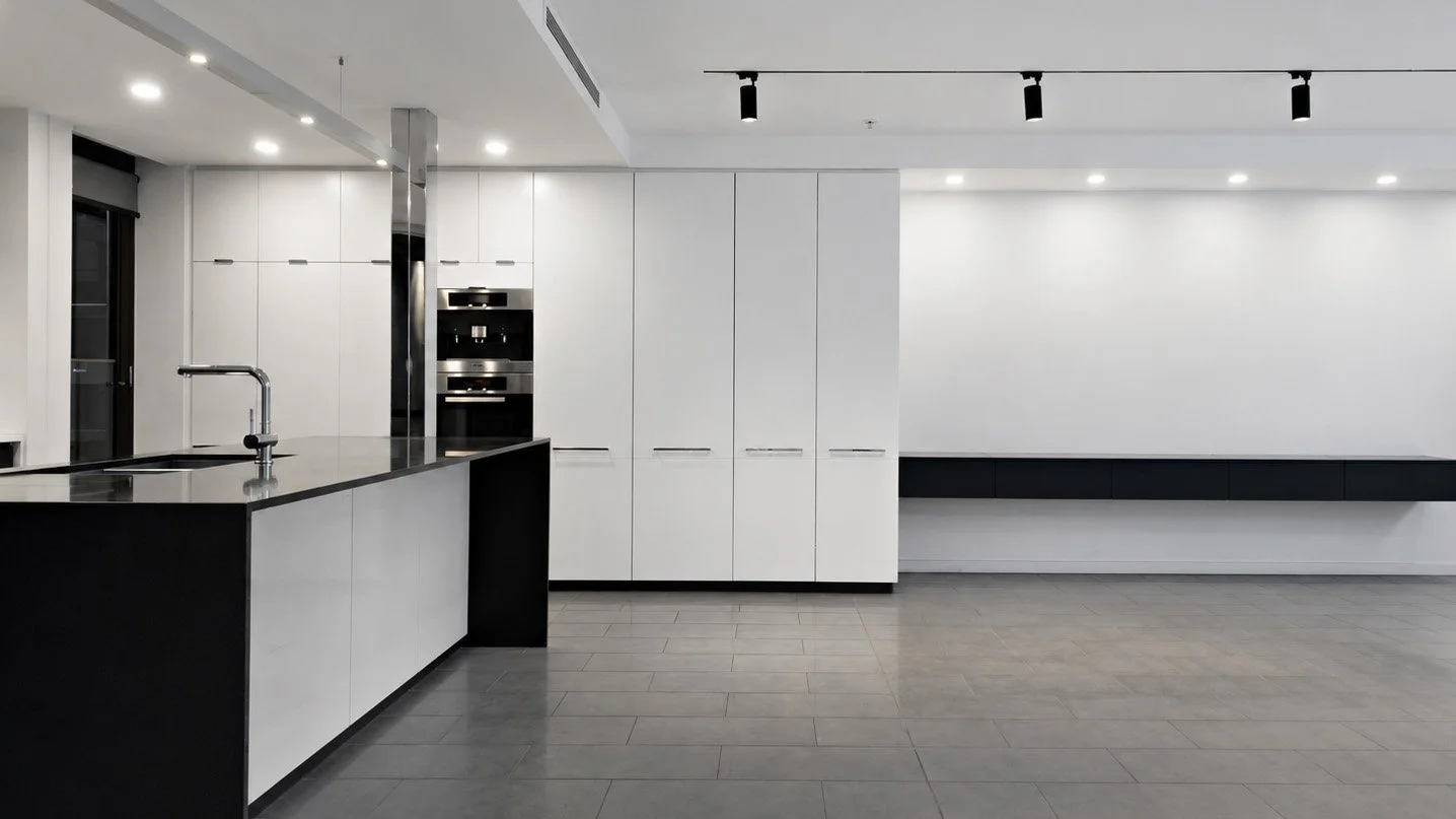 The kitchen before the design — white cabinetry, black benchtop and grey tiled floor