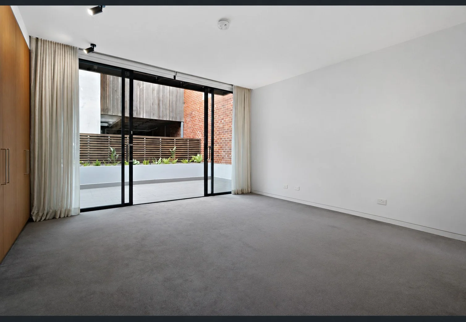 A bedroom before the design — grey carpet, timber wardrobe and sliding doors to the courtyard