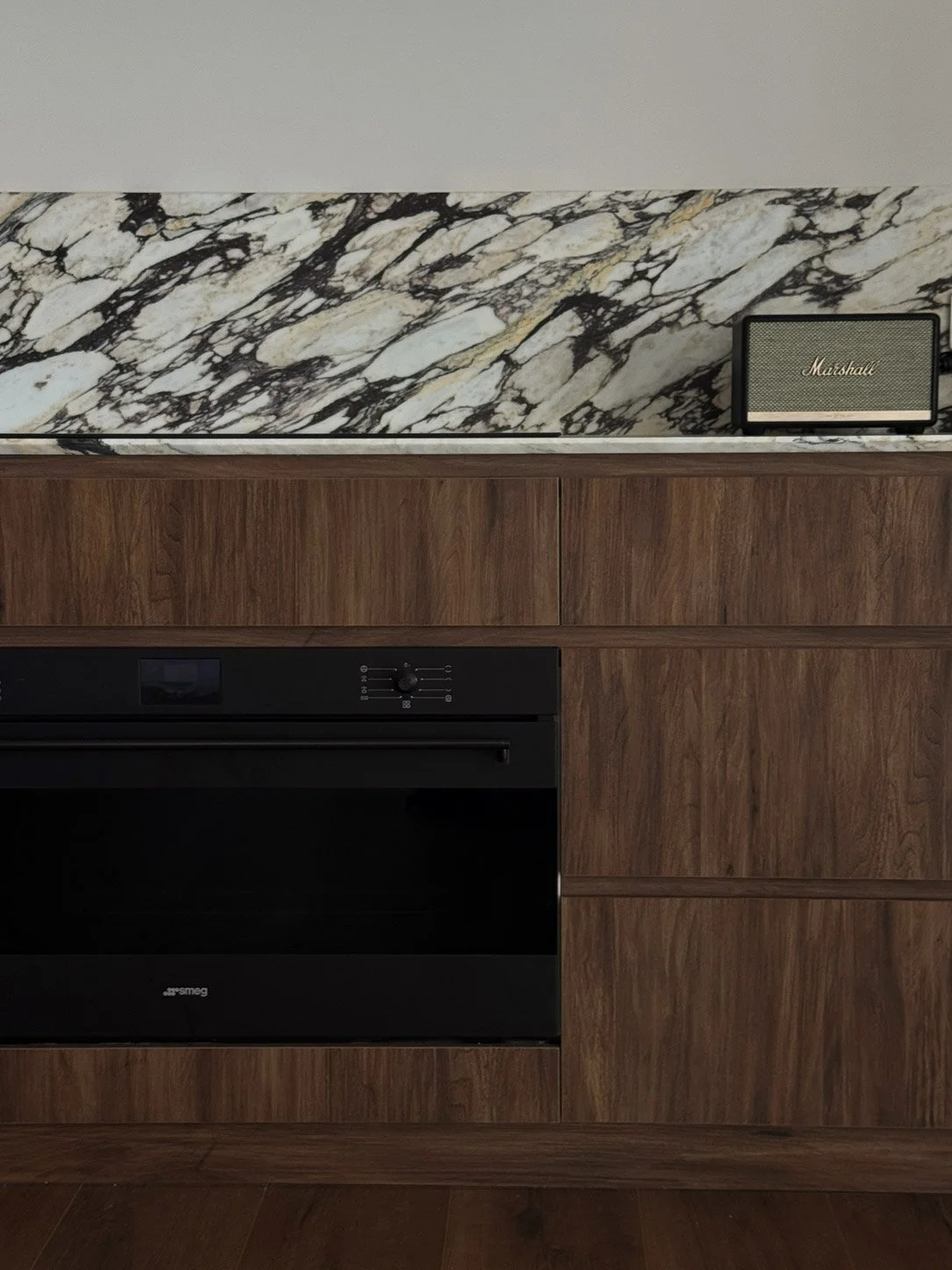 Kitchen detail — Calacatta Monet splashback above walnut cabinetry, a black oven and a Marshall speaker on top