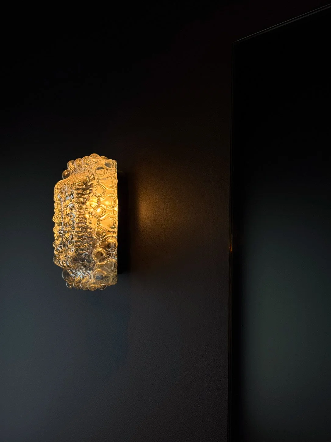 Textured amber glass sconce lighting a wall painted deep aubergine
