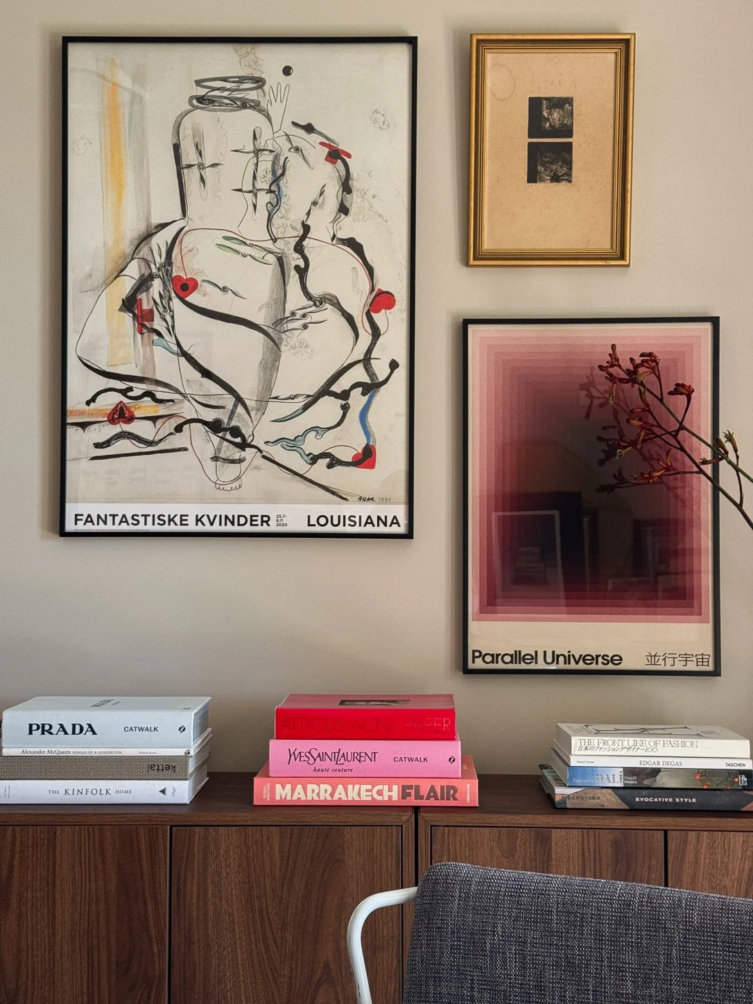 Gallery wall of exhibition posters and a gold-framed etching above a walnut credenza of fashion books