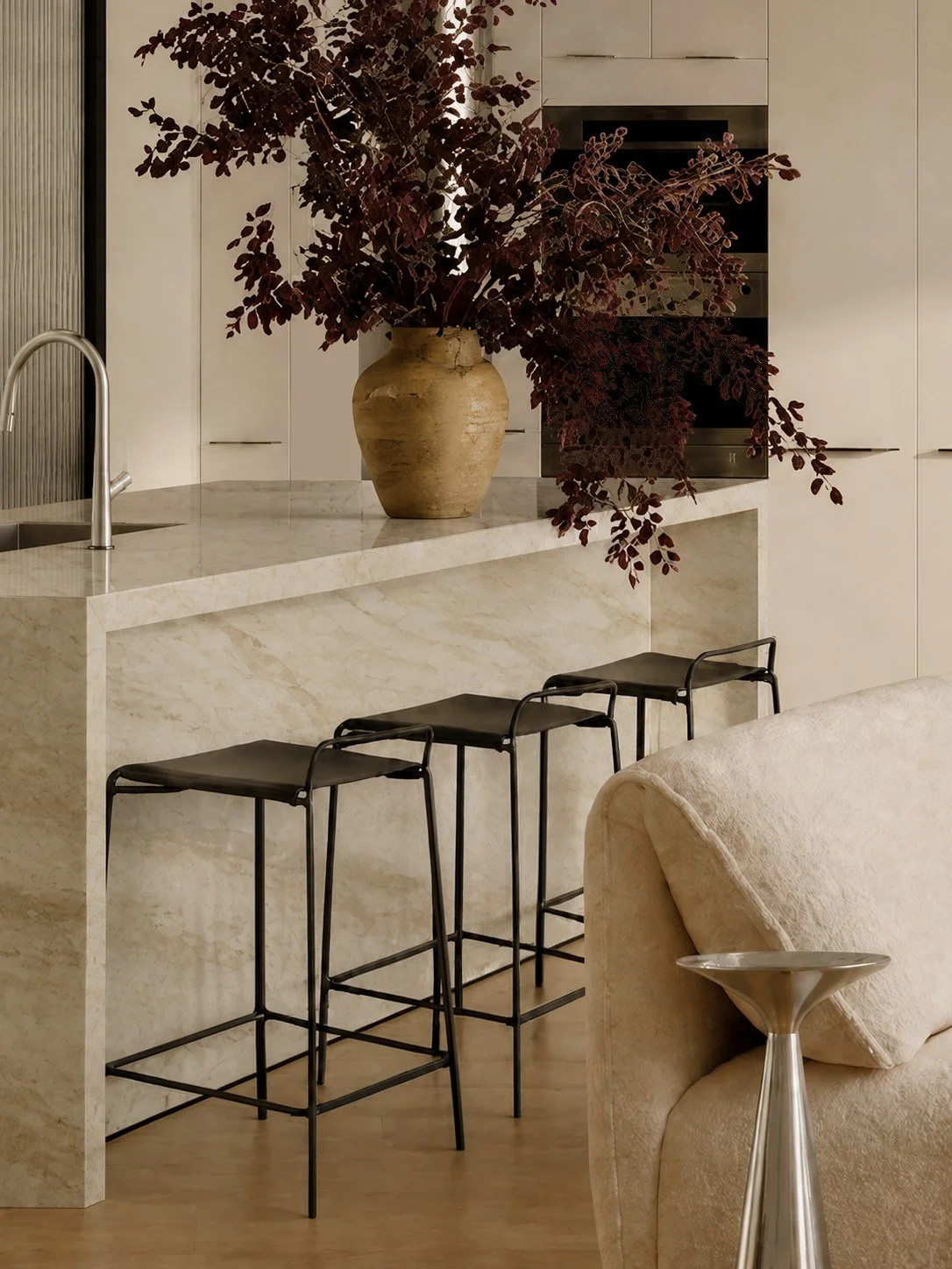 Kitchen with a Taj Mahal marble island, black leather stools and an urn of burgundy foliage