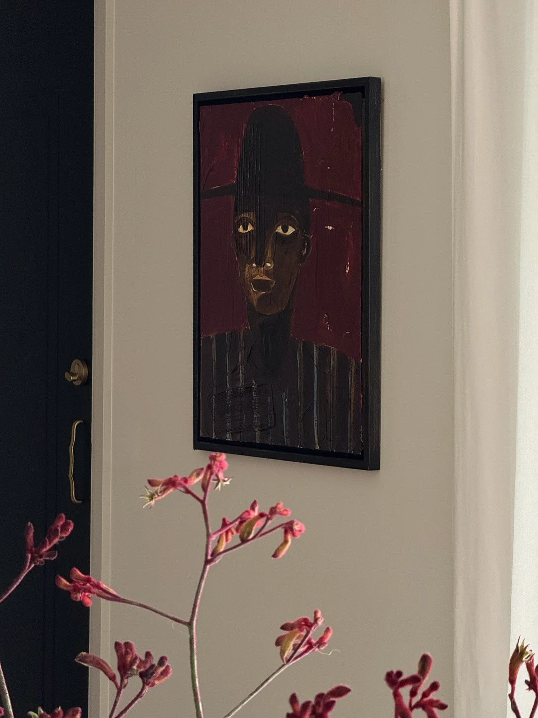 Dark portrait painting in a black frame beside the entry door, kangaroo paw in the foreground