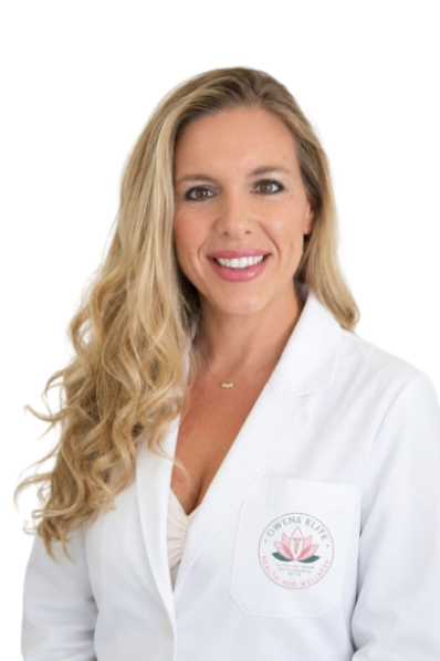 Portrait of a woman with long, curly blonde hair wearing a white lab coat with a pink logo on the left chest.