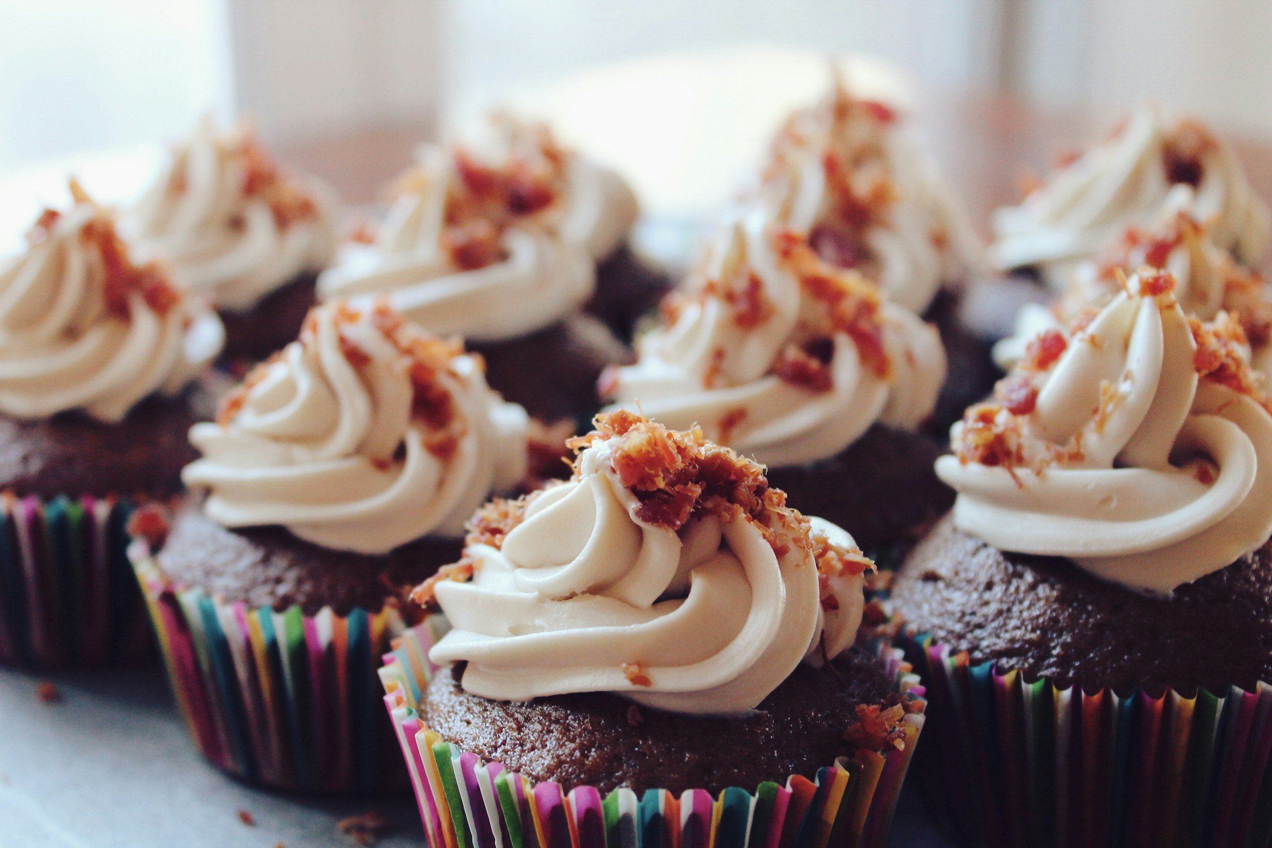 Chocolate cupcakes topped with vanilla frosting and bacon bits in colorful paper cupcake liners.