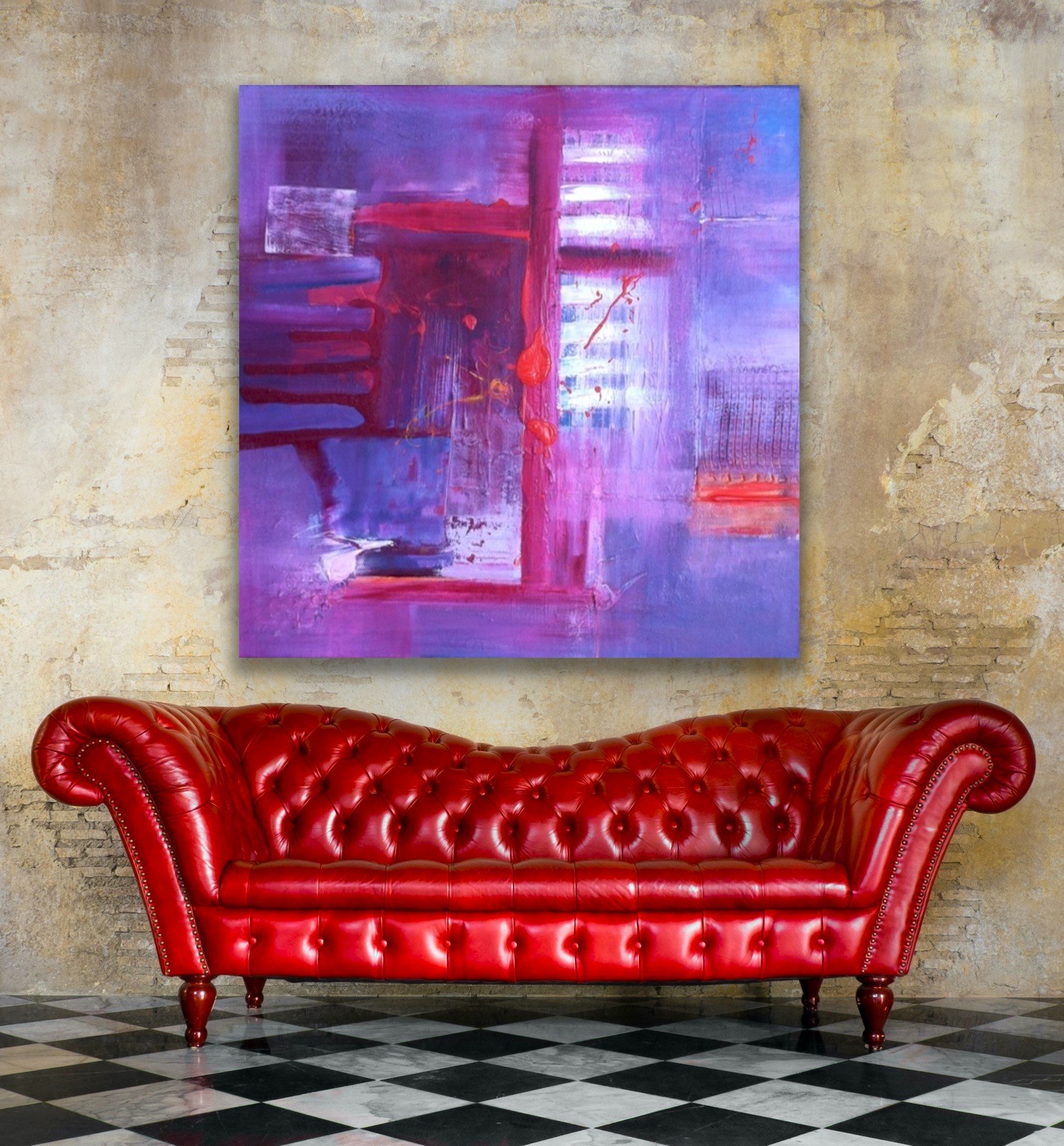 A red leather tufted Chesterfield sofa with rolled arms and wooden legs in front of a textured beige wall. Behind the sofa, a large abstract purple painting with red and white accents is hung on the wall. The floor features a black and white checkered pattern.
