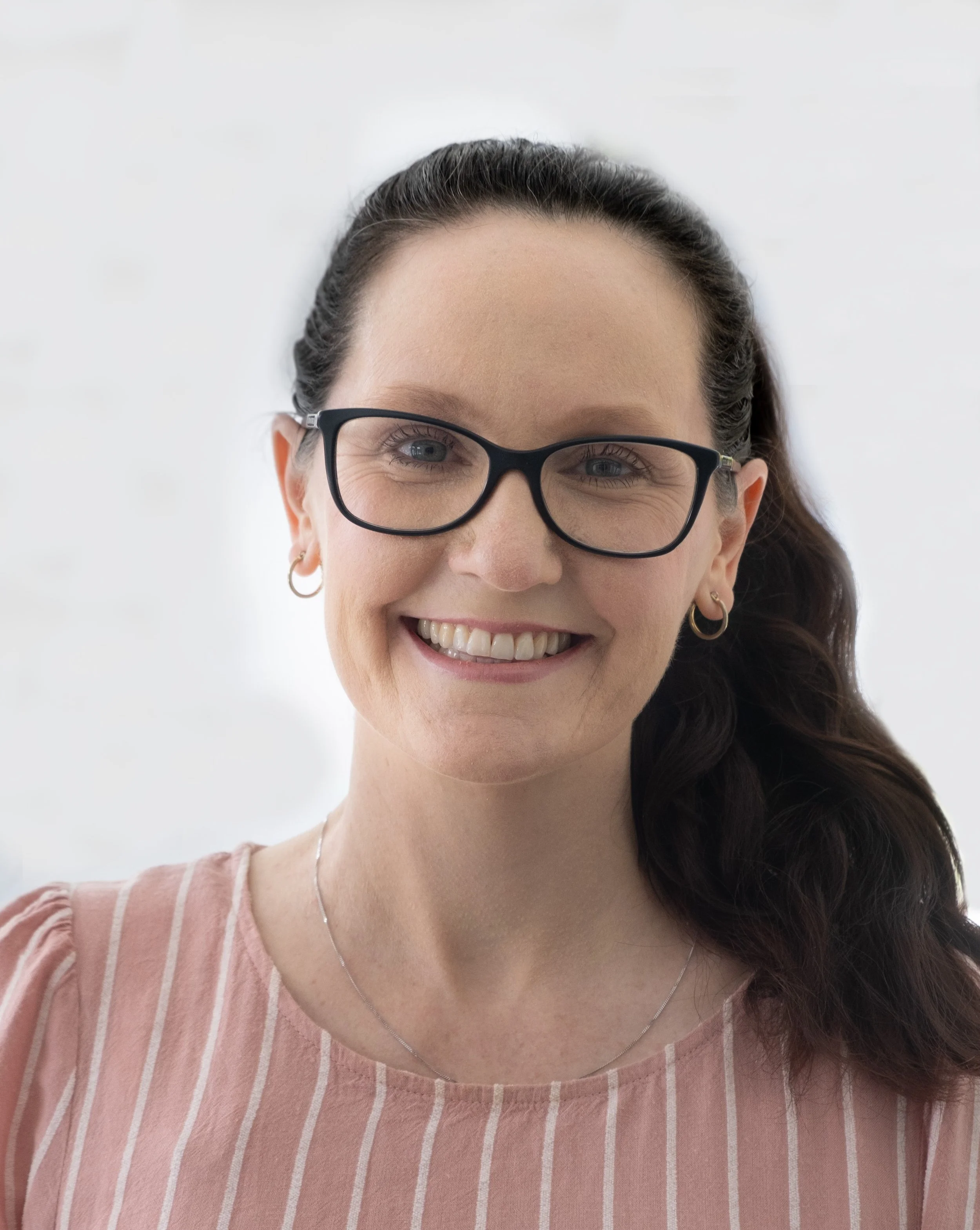 Close-up of a woman smiling, wearing glasses and a pink striped shirt.