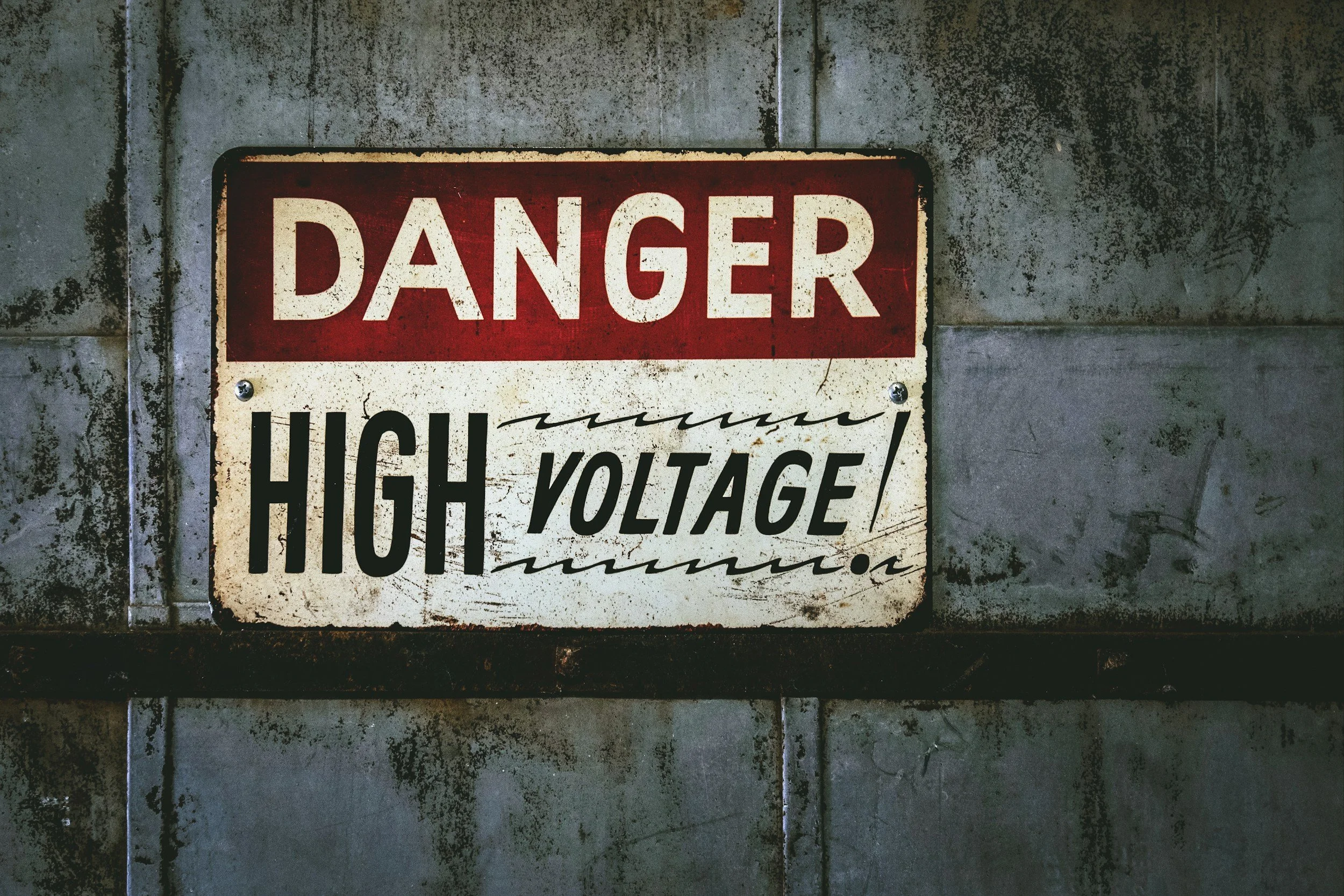 A weathered warning sign on a concrete wall warning of high voltage danger.