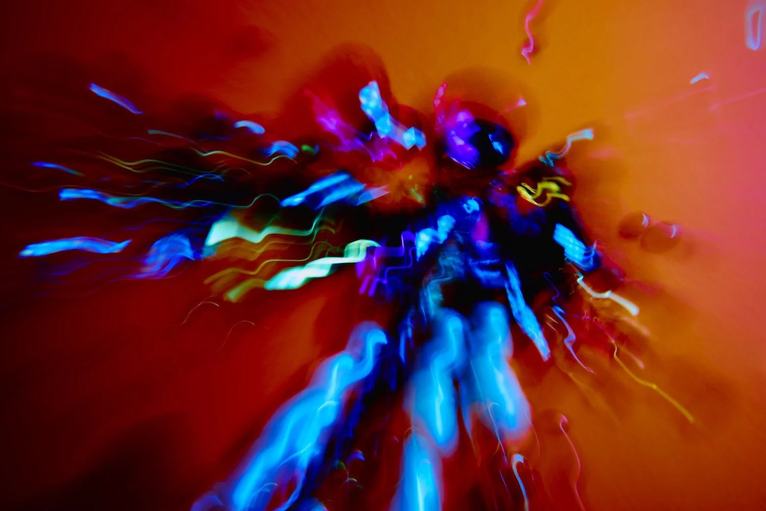 Imagem com luzes coloridas, principalmente azuis, verdes, roxas e amarelas, em movimento, criando um efeito de foco desfoque contra um fundo laranja, do catalogo Spectra Nova