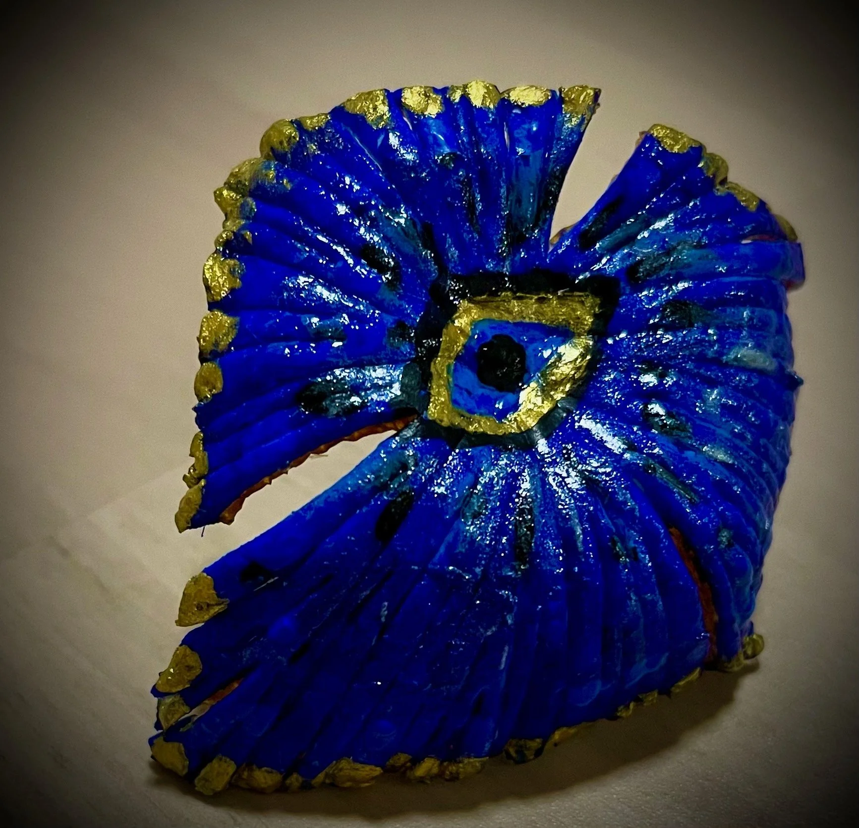 Close-up of a pressed and painted blue citrus rind with gold accents on the edges and venation, viewed from the side.