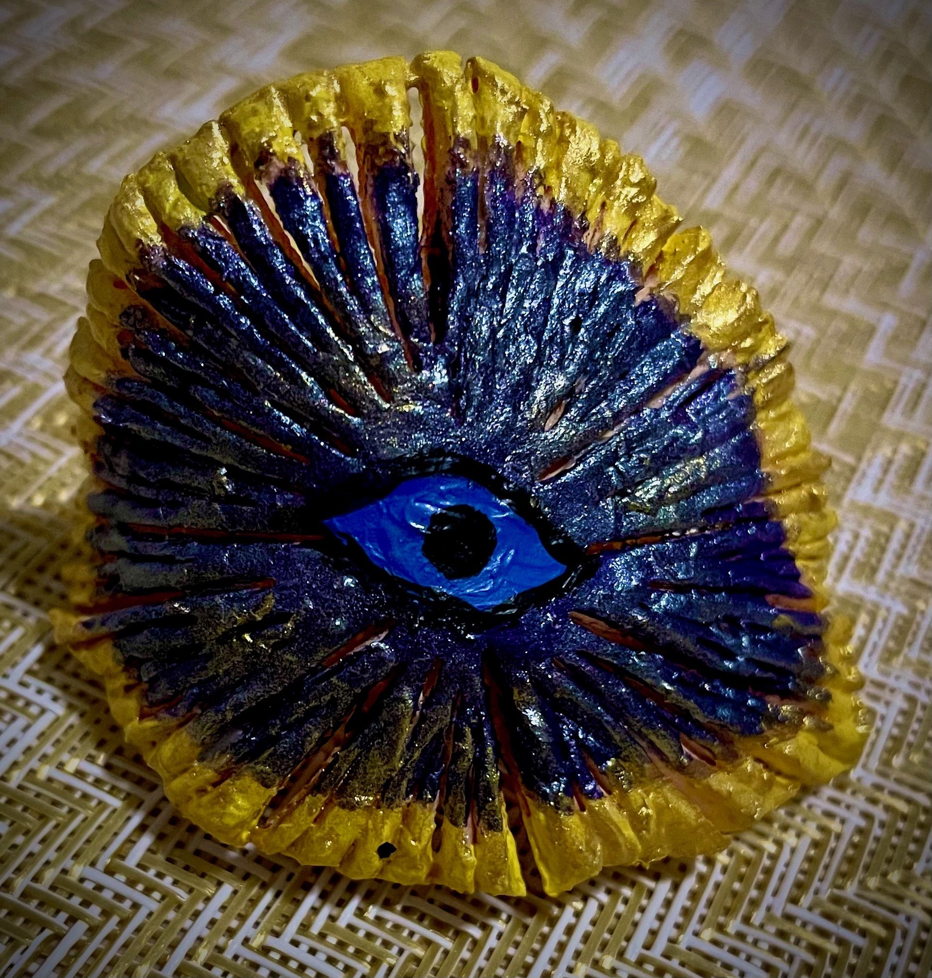 Close-up of a shiny, metallic yellow and blue citrus rind object, with intricate details, placed on a woven surface.