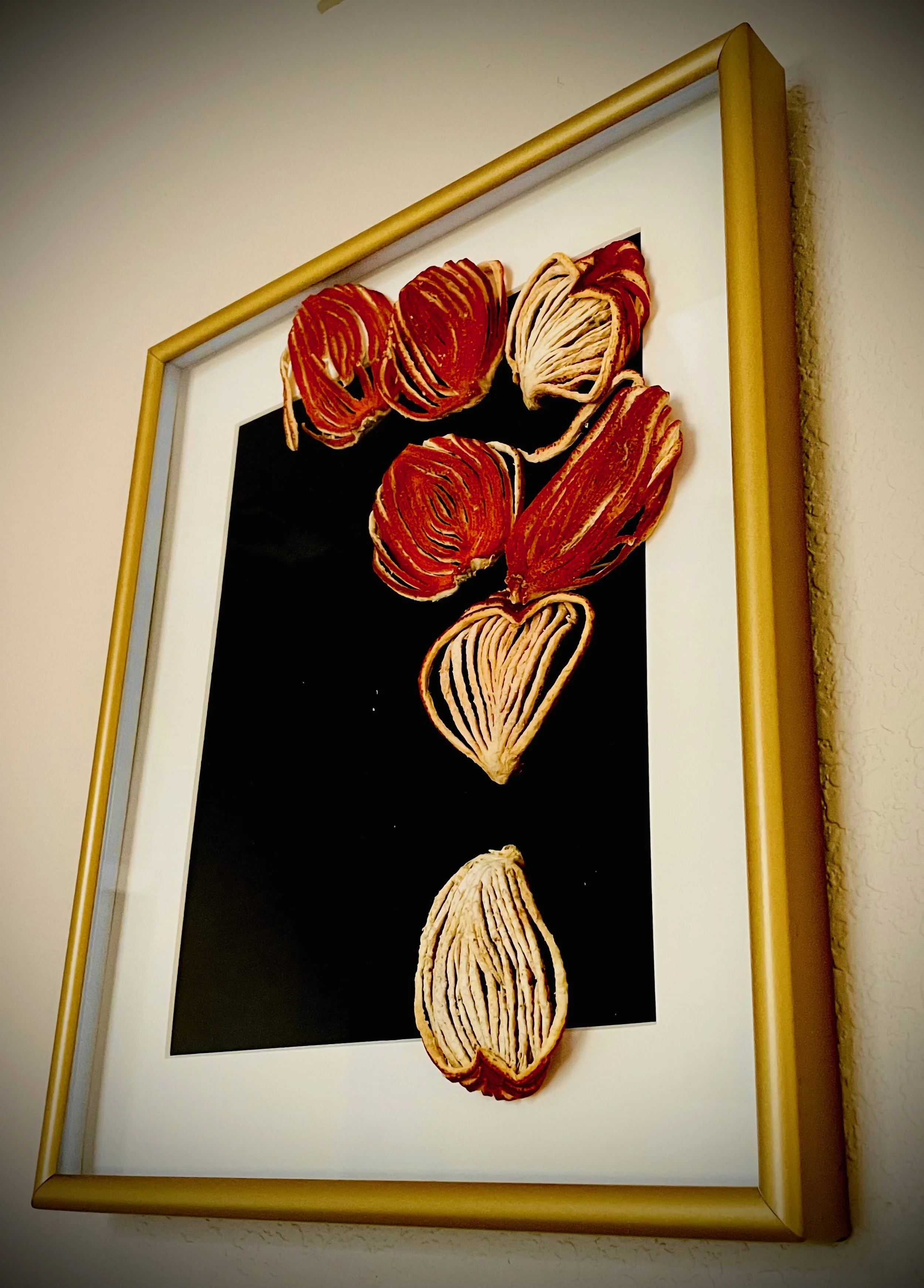 Frame with a black background and carved citrus rind pieces arranged vertically.