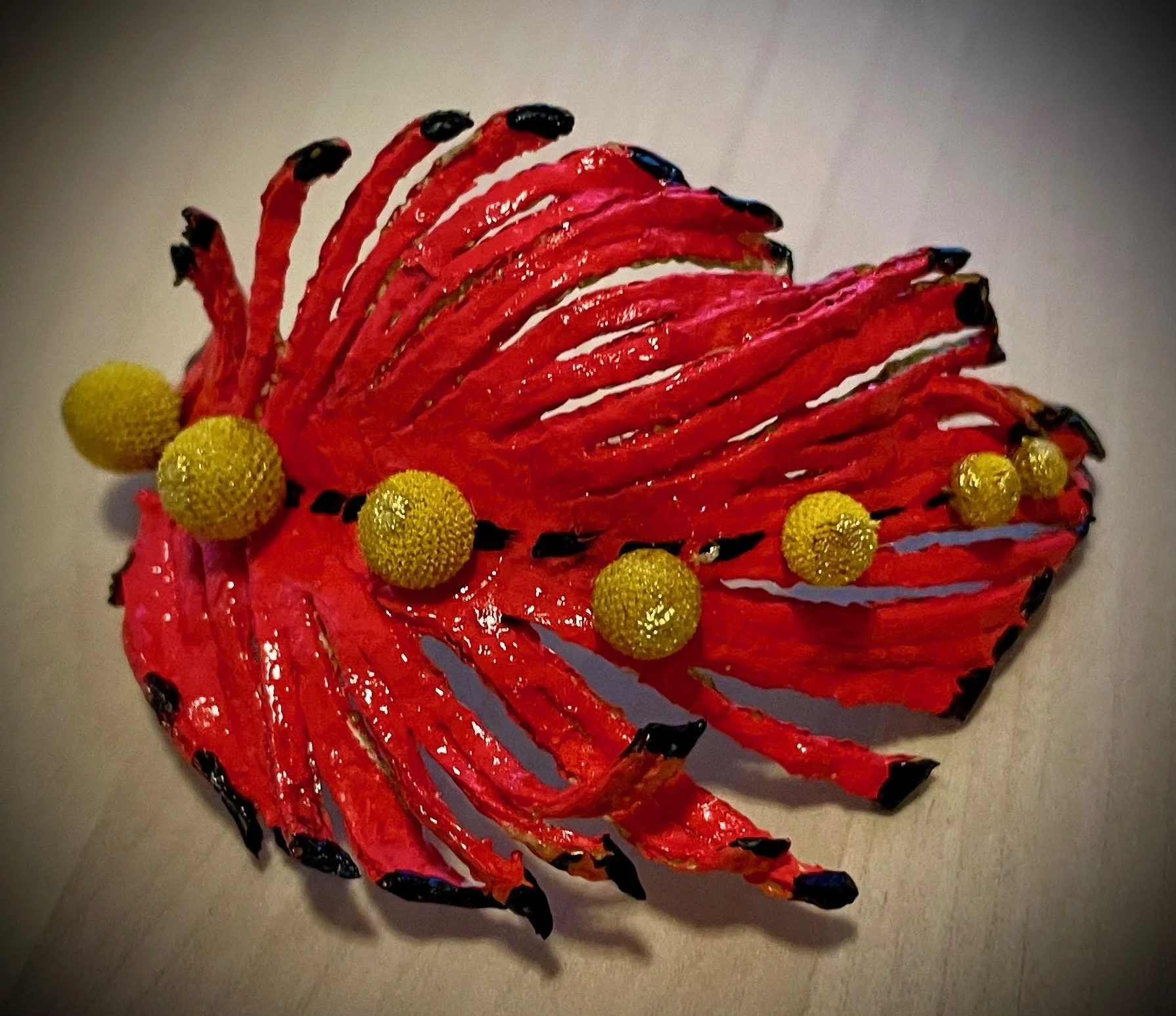 A decorative citrus rind piece depicting a red fish with black-tipped fins and yellow textured spheres on its body.