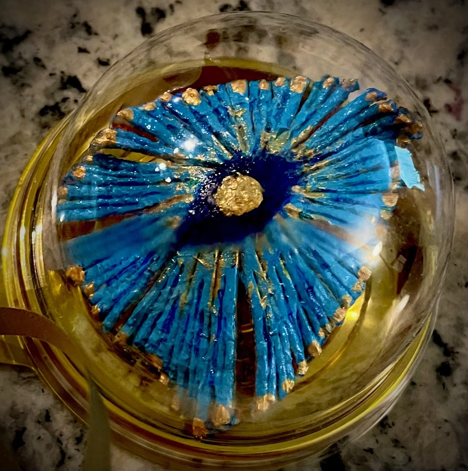 A citrus rind with a blue decorative flower-like object with gold accents at the center, sitting on a dark granite surface.