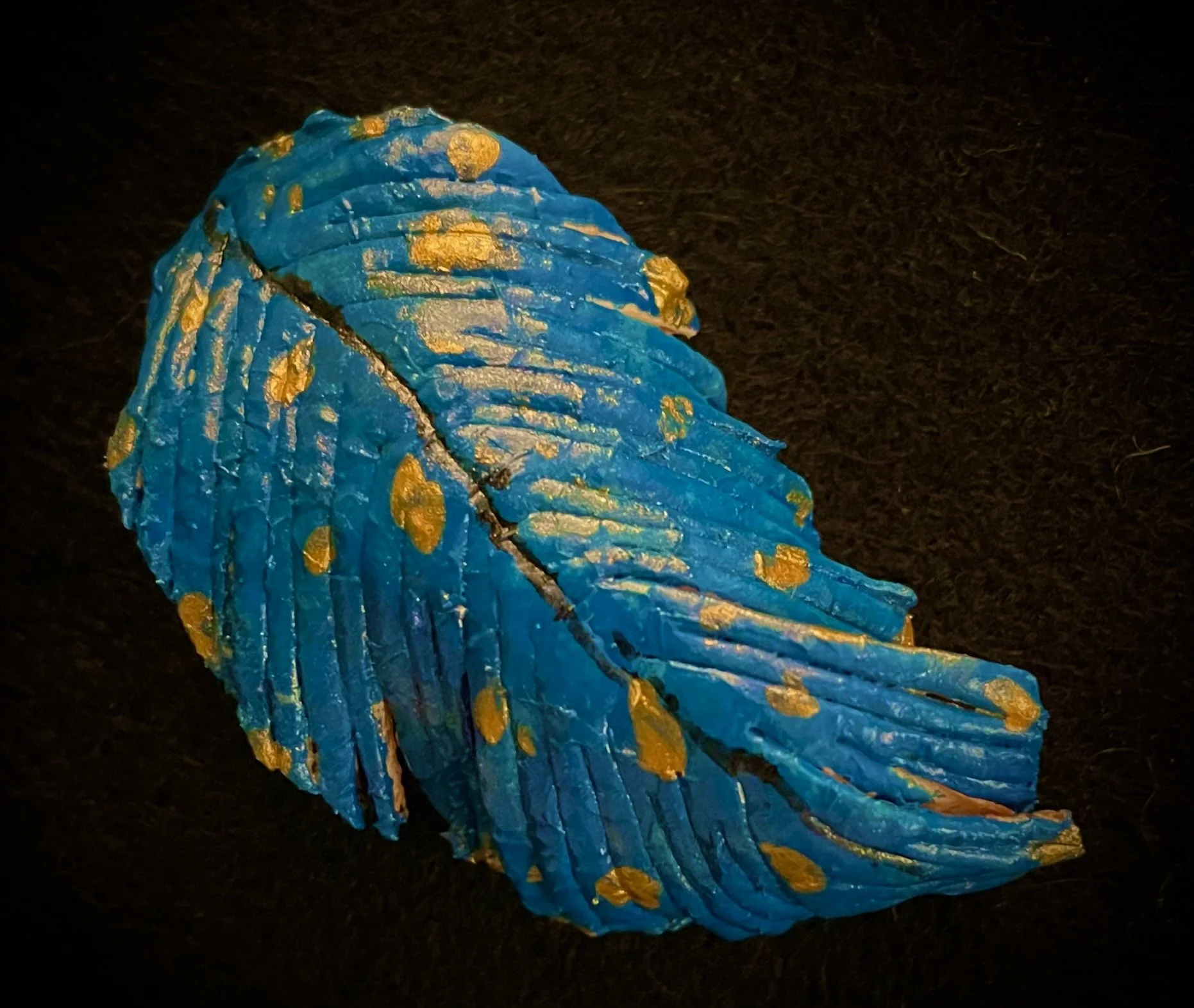 A large seashell shaped citrus rind with a bright blue surface and gold spots on a dark background.