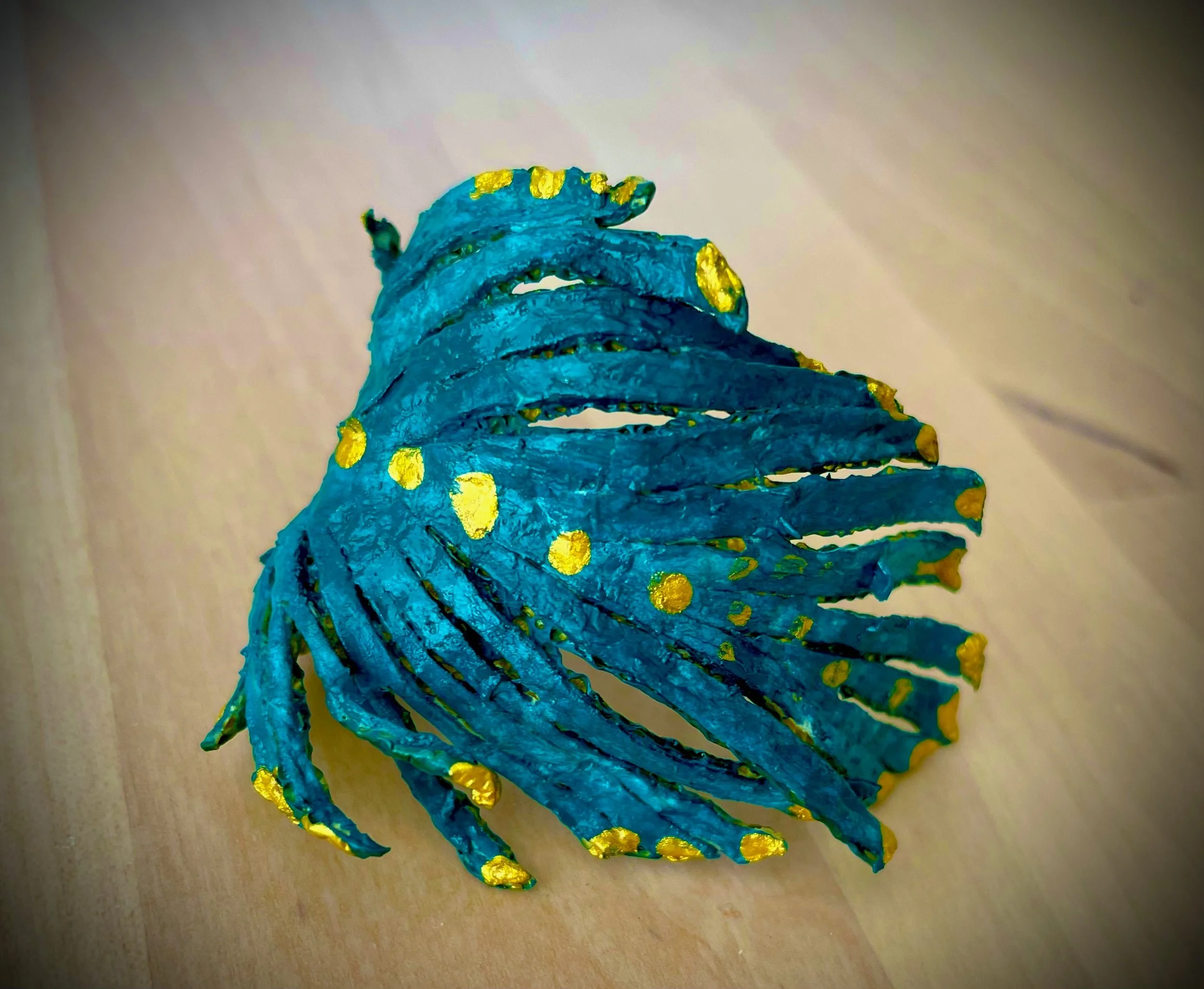 A citrus rind sculpture painted in blue with gold dots, mounted on a wooden surface.