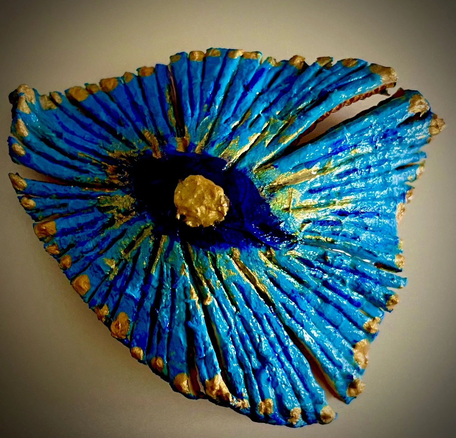 A decorative citrus rind art piece resembling a seashell with a blue surface accented with gold details.