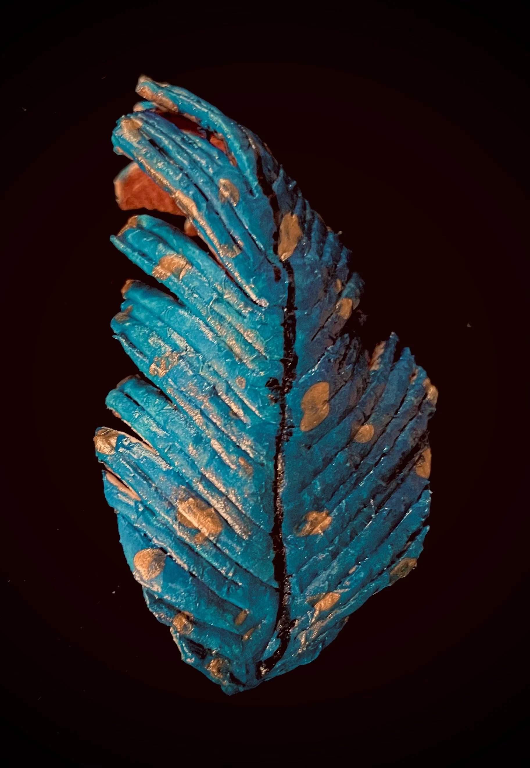 A sculpture of a blue citrus rind with gold accents, set against a dark background.
