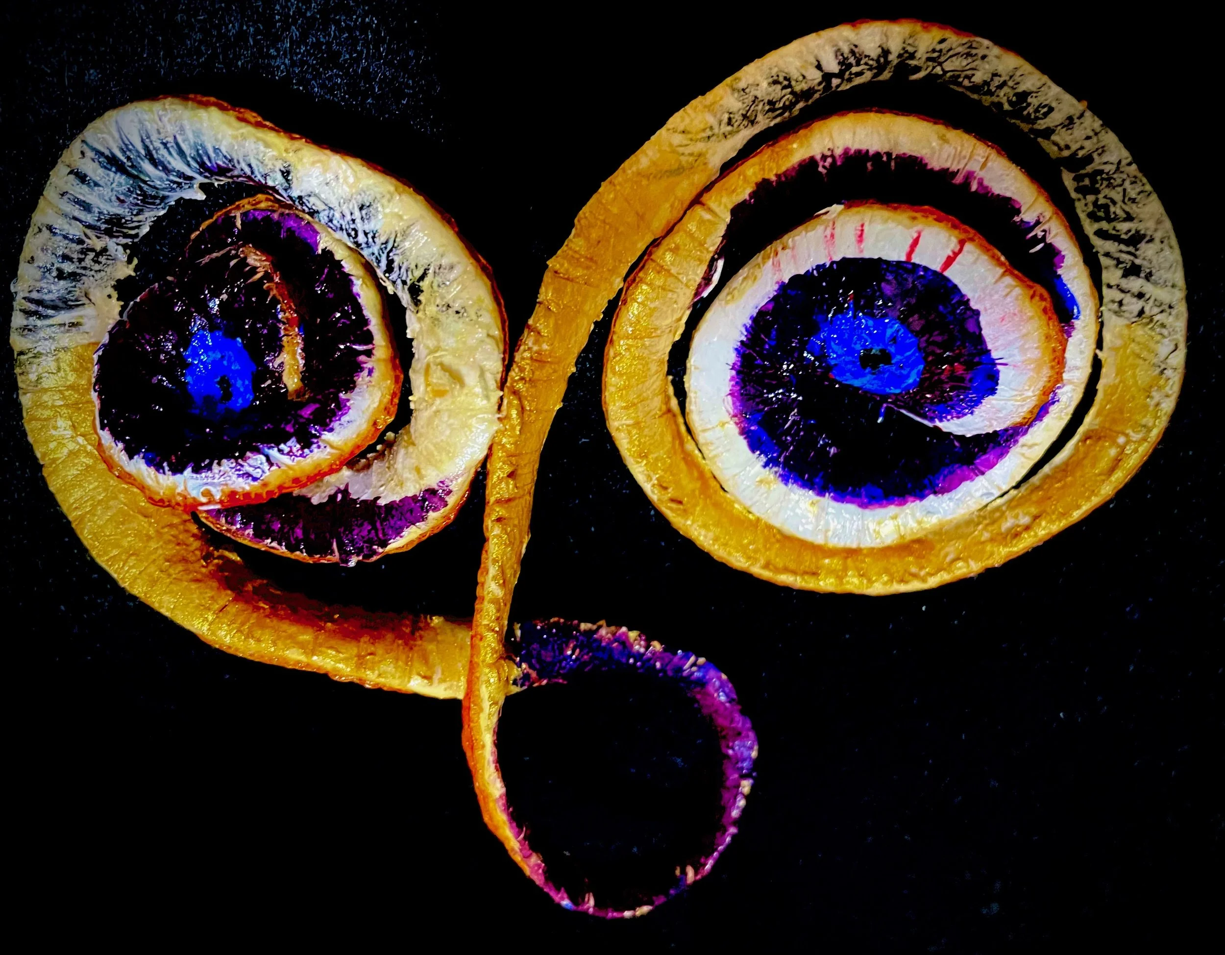 Close-up of dried citrus rinds with vibrant purple, blue, white, and orange colors on a black background.