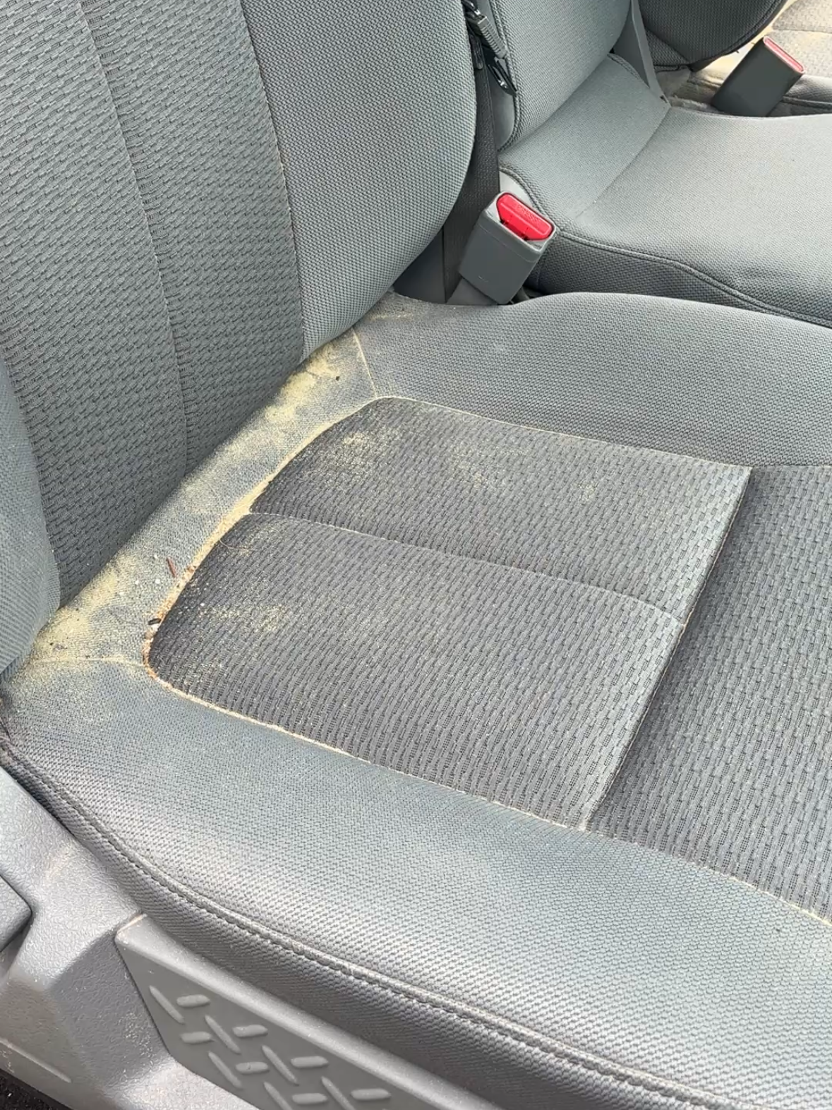 A gray car seat with dirt, dust, and debris accumulated in the creases and corners.