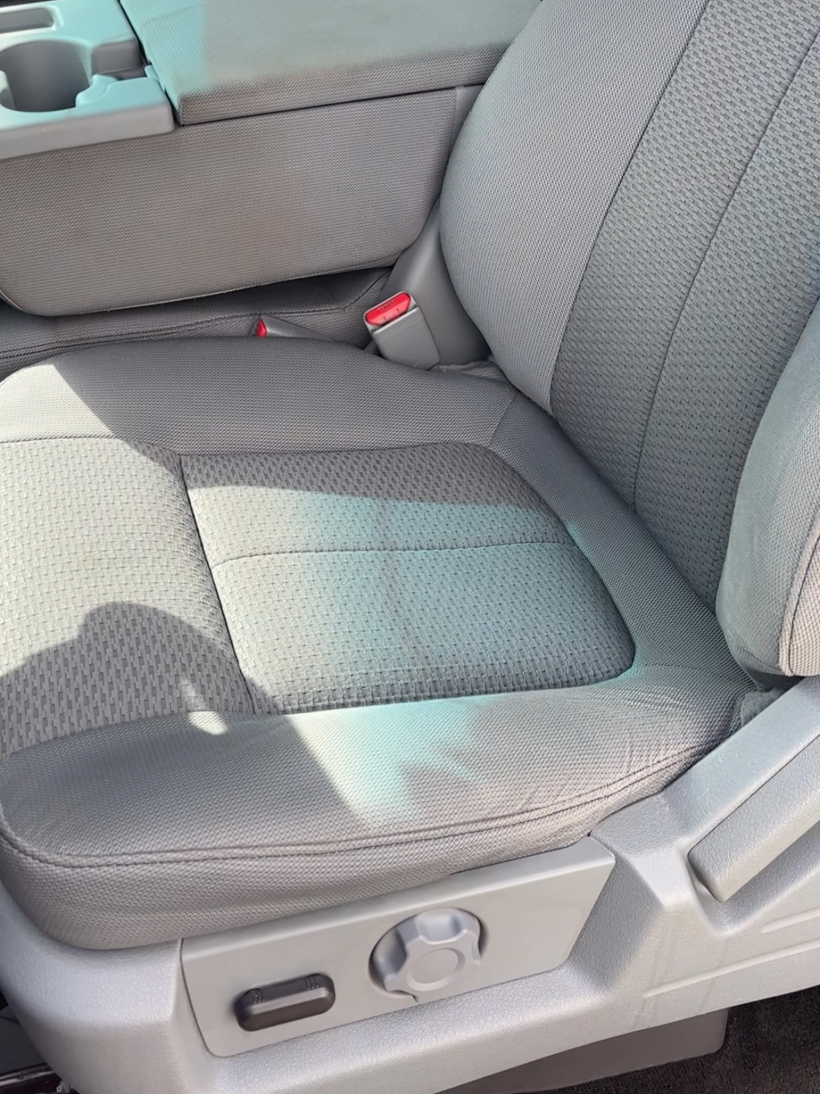 Gray fabric car seat with manual adjustments and a textured seat surface, located in a vehicle's interior.