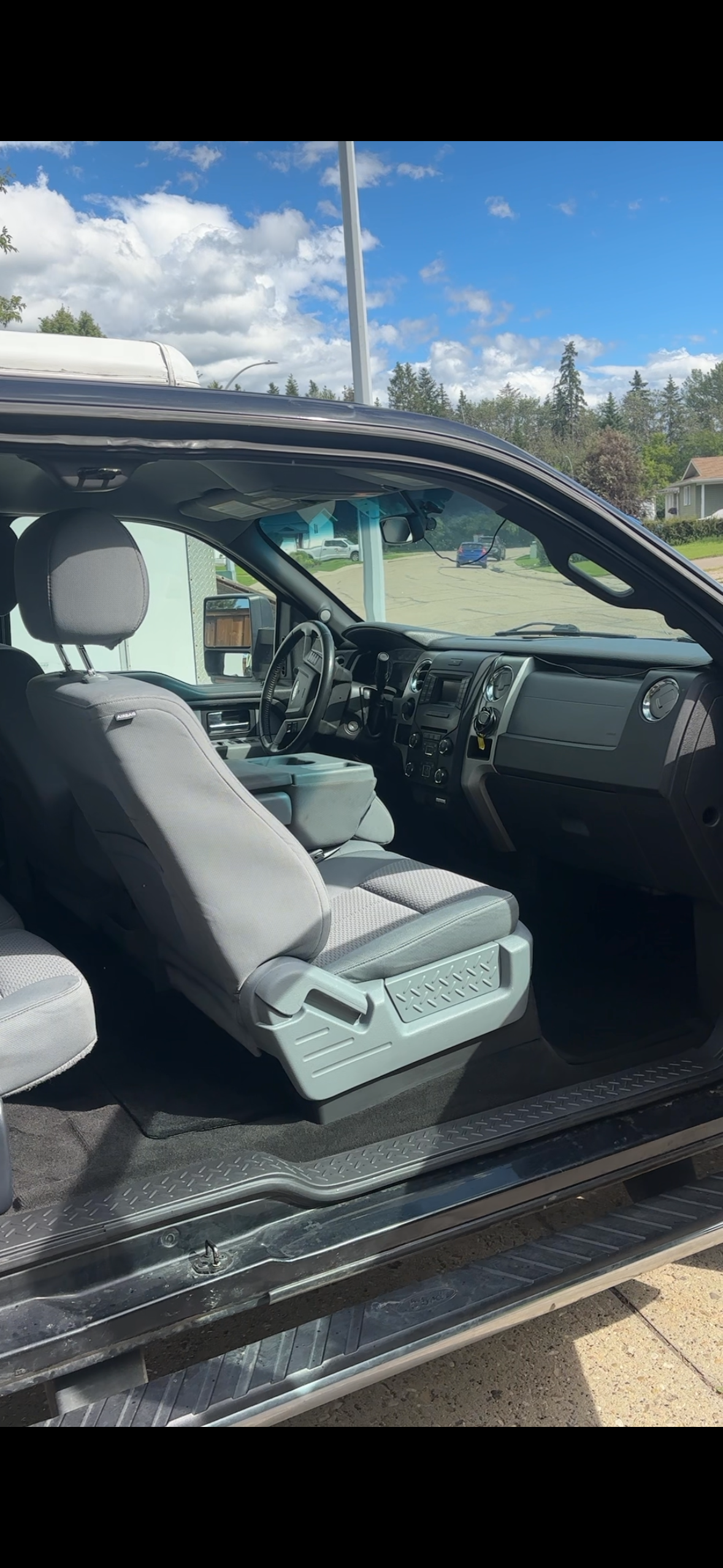 Interior view of a pickup truck with gray seats and dashboard, parked on a street under a partly cloudy sky.