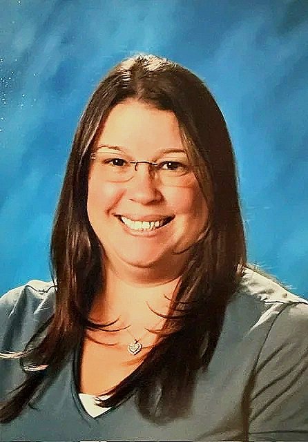 Portrait of a woman with long, dark hair, wearing glasses, smiling, against a blue background.