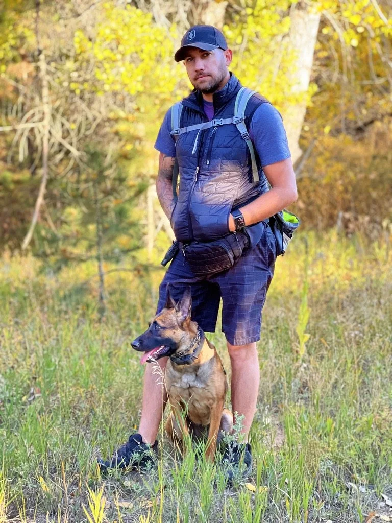 Mitch standing outdoors with a tan and black dog on a leash.