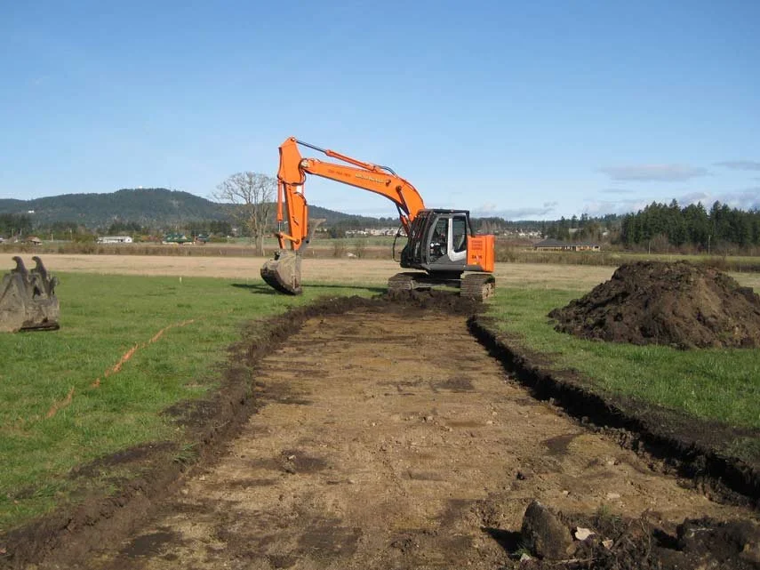Excavator working on a construction project in a grassy field on a clear day.