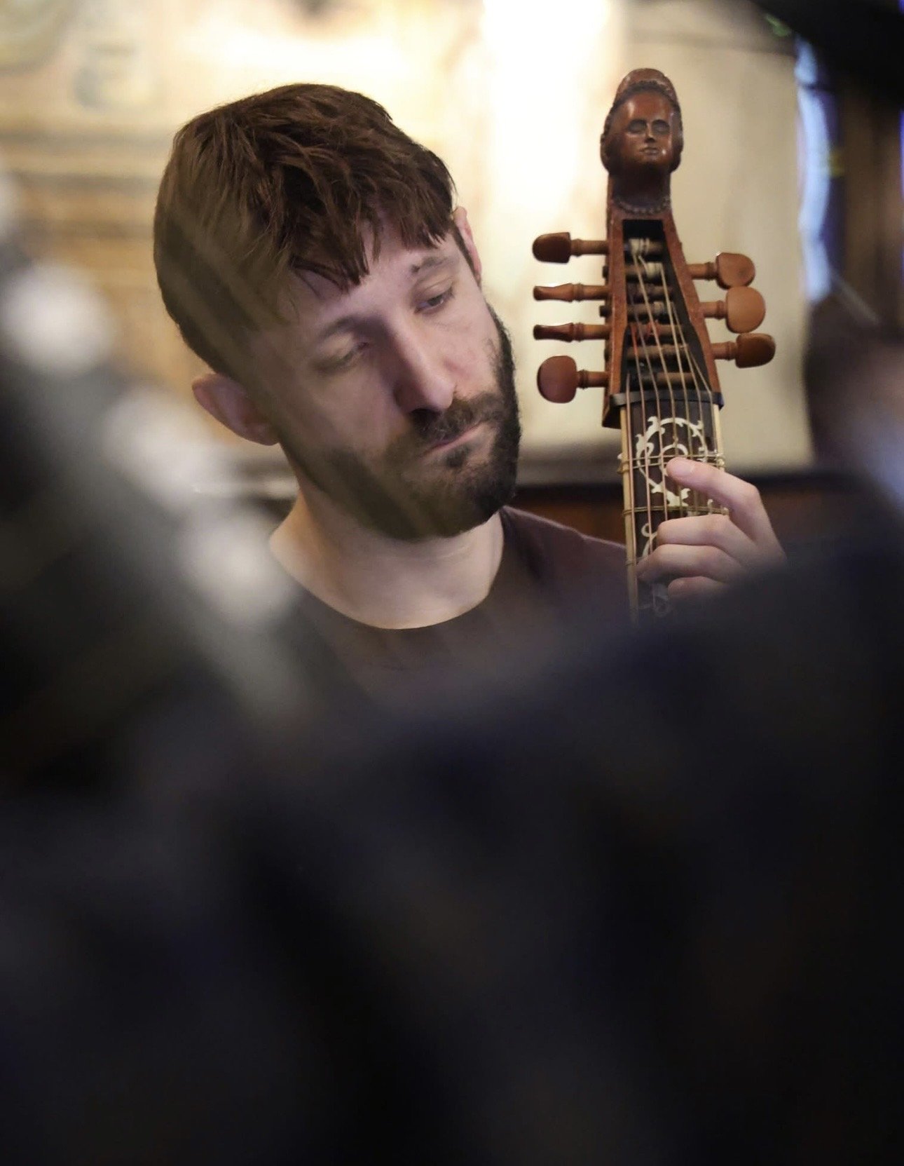 A man with reddish hair and beard playing a guitar with a carved head sculpt of a woman on the headstock.