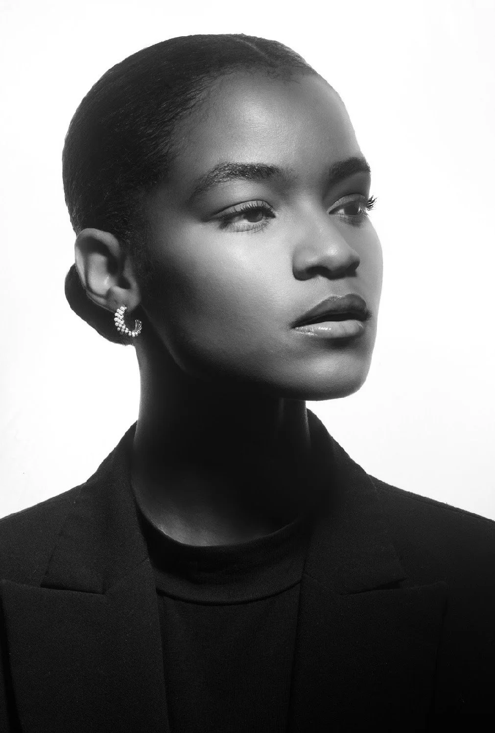 Black and white portrait of a woman with short hair, wearing a black blazer and a hoop earring, looking to the side.