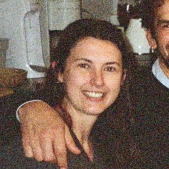 A young woman smiling with dark hair, in a casual indoor setting.