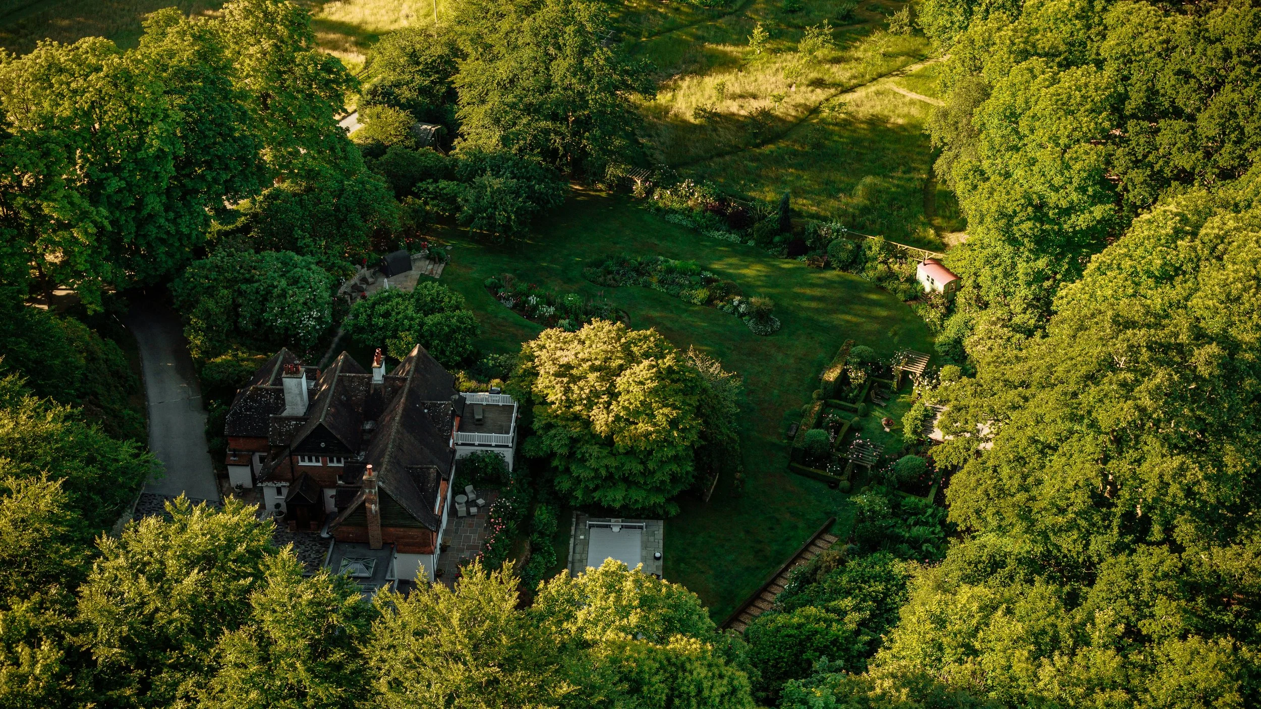 Aerial view of a house with a garden, surrounded by large trees and lush greenery.