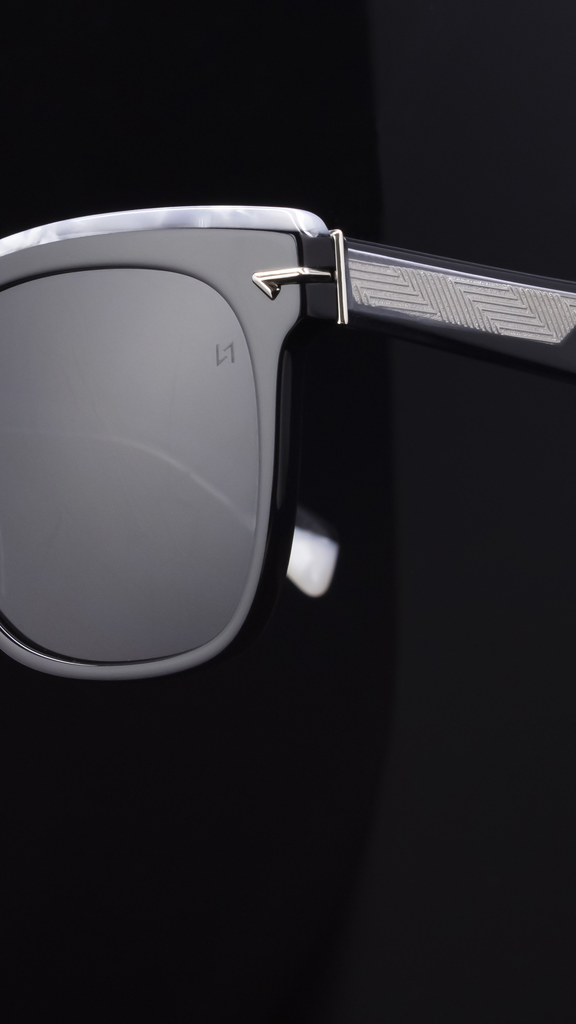 Close-up of a sunglass with Acetate details and silver decor against a black background.