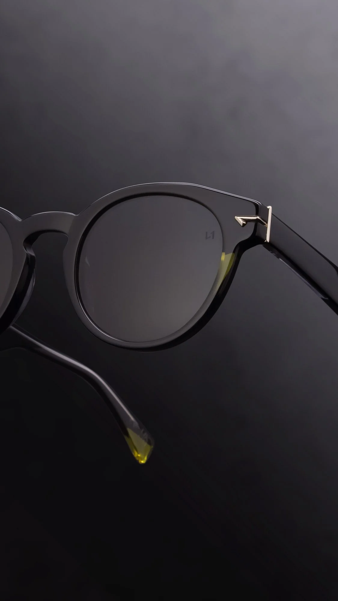 A pair of black sunglasses with round lenses and metallic accents on the frame, resting on a dark surface.