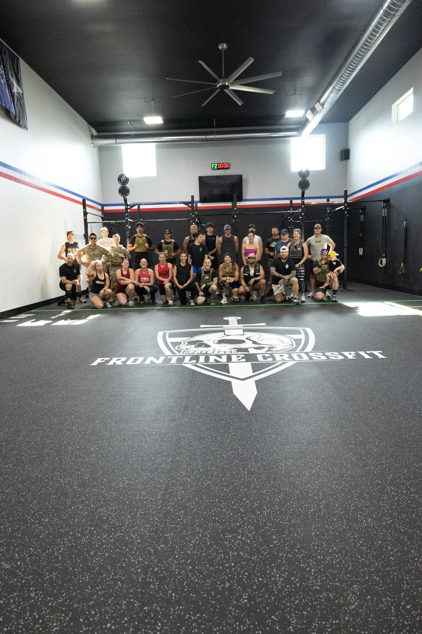 Group of people posing in a CrossFit gym with the Frontline CrossFit logo on the floor.