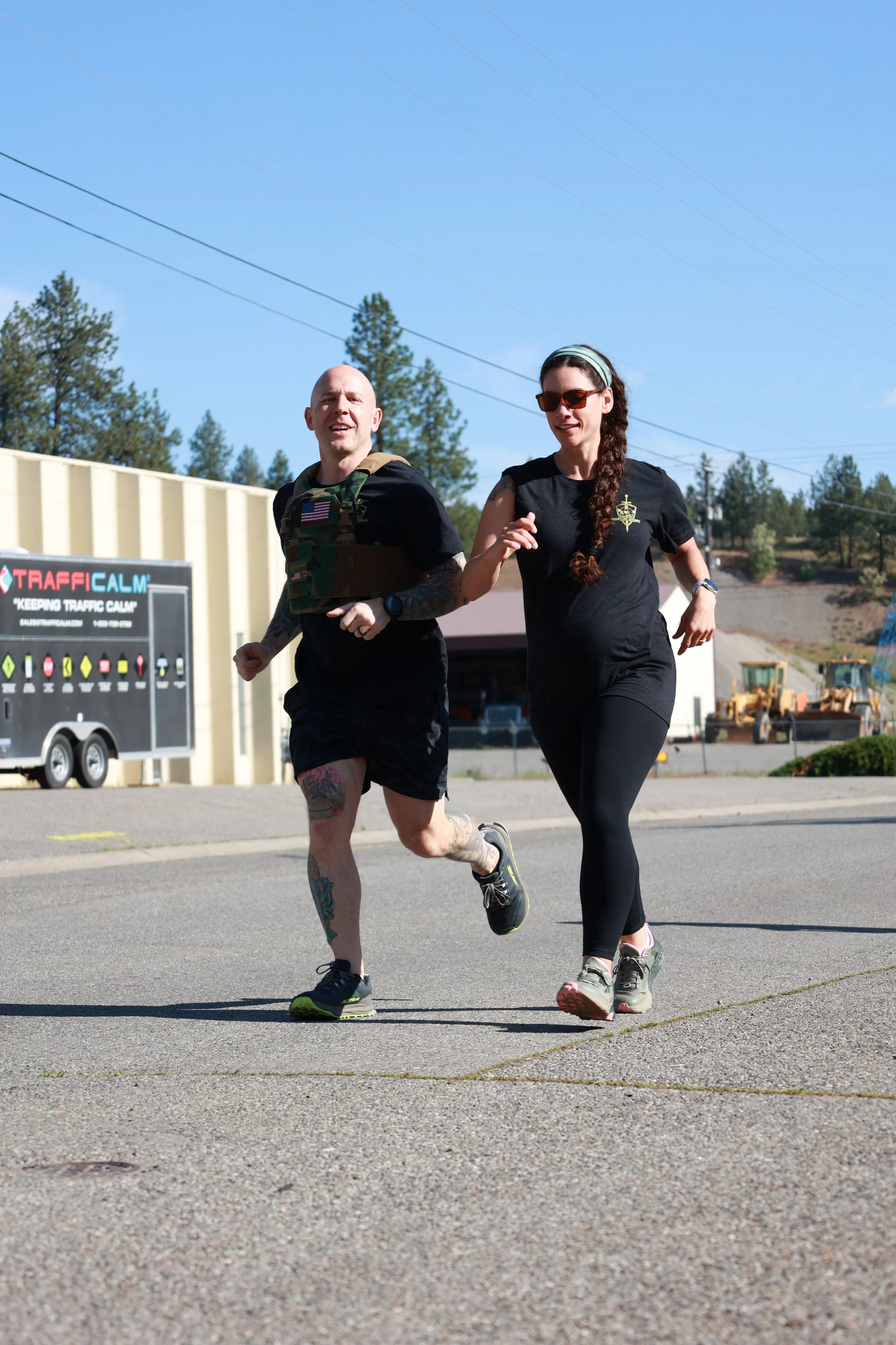 Two people jogging outdoors on a clear day, with a sign reading 'Traffic Calm' and a trailer nearby.