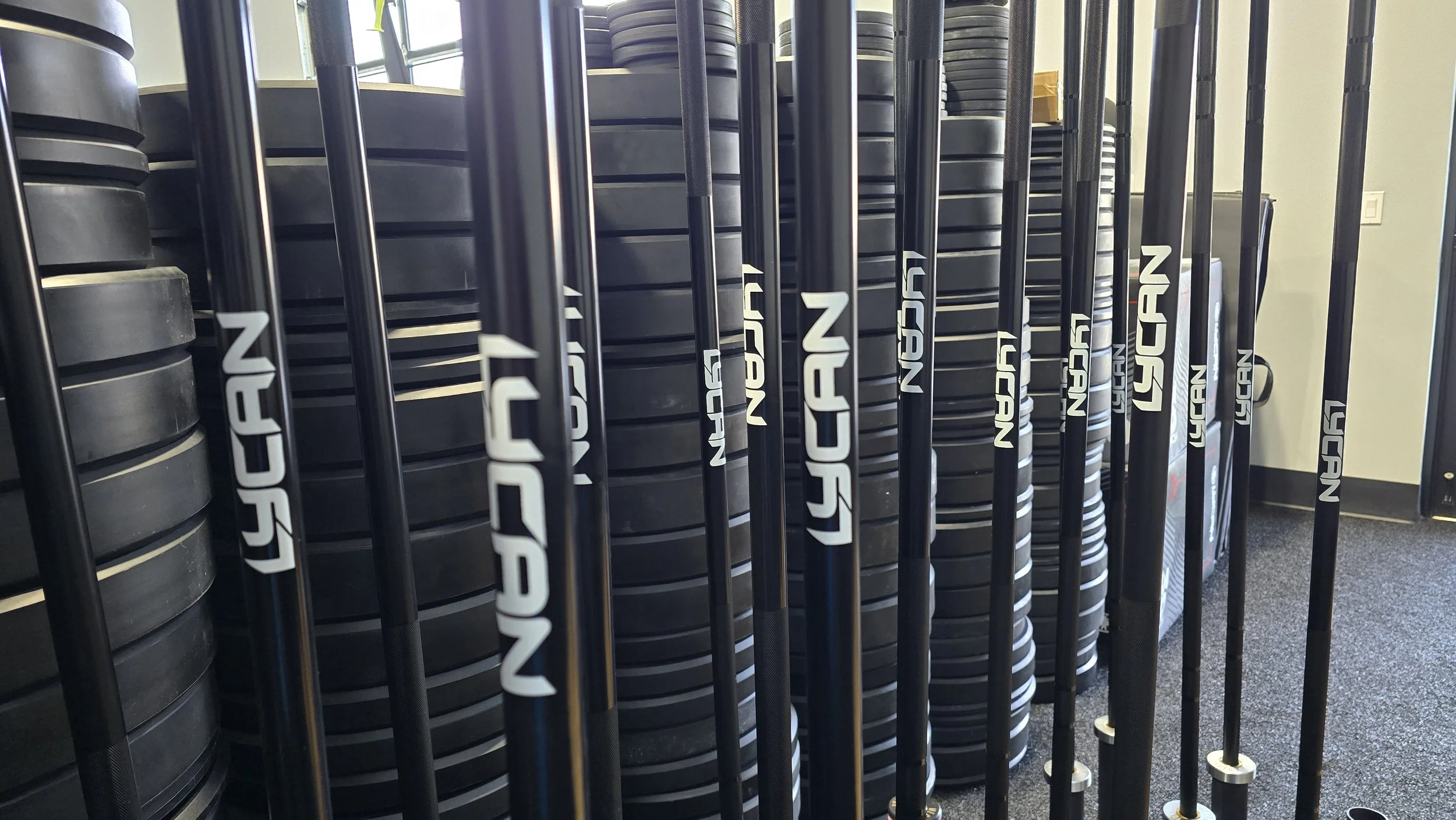 A rack of black golf club shafts with the brand name 'NECGAN' printed on them, standing next to a wall with cookie sheets or similar items stacked vertically.