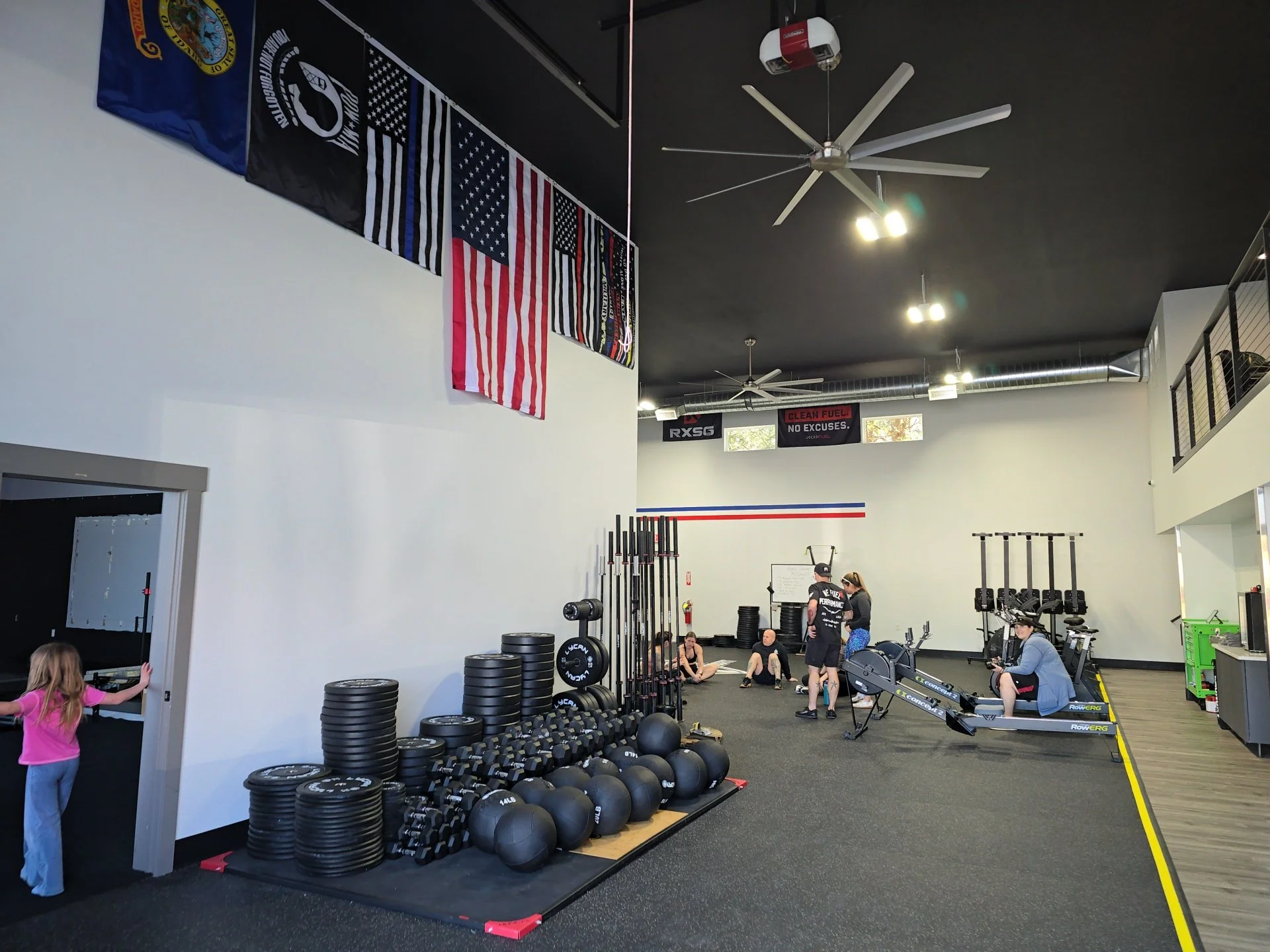 Interior of a gym with American flags and blue line flags on the wall, various workout equipment, and people exercising and socializing.