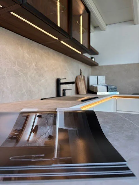 Planche de design ou de planification sur un plan de travail de cuisine moderne avec armoires en bois foncé et comptoir en marbre beige.
