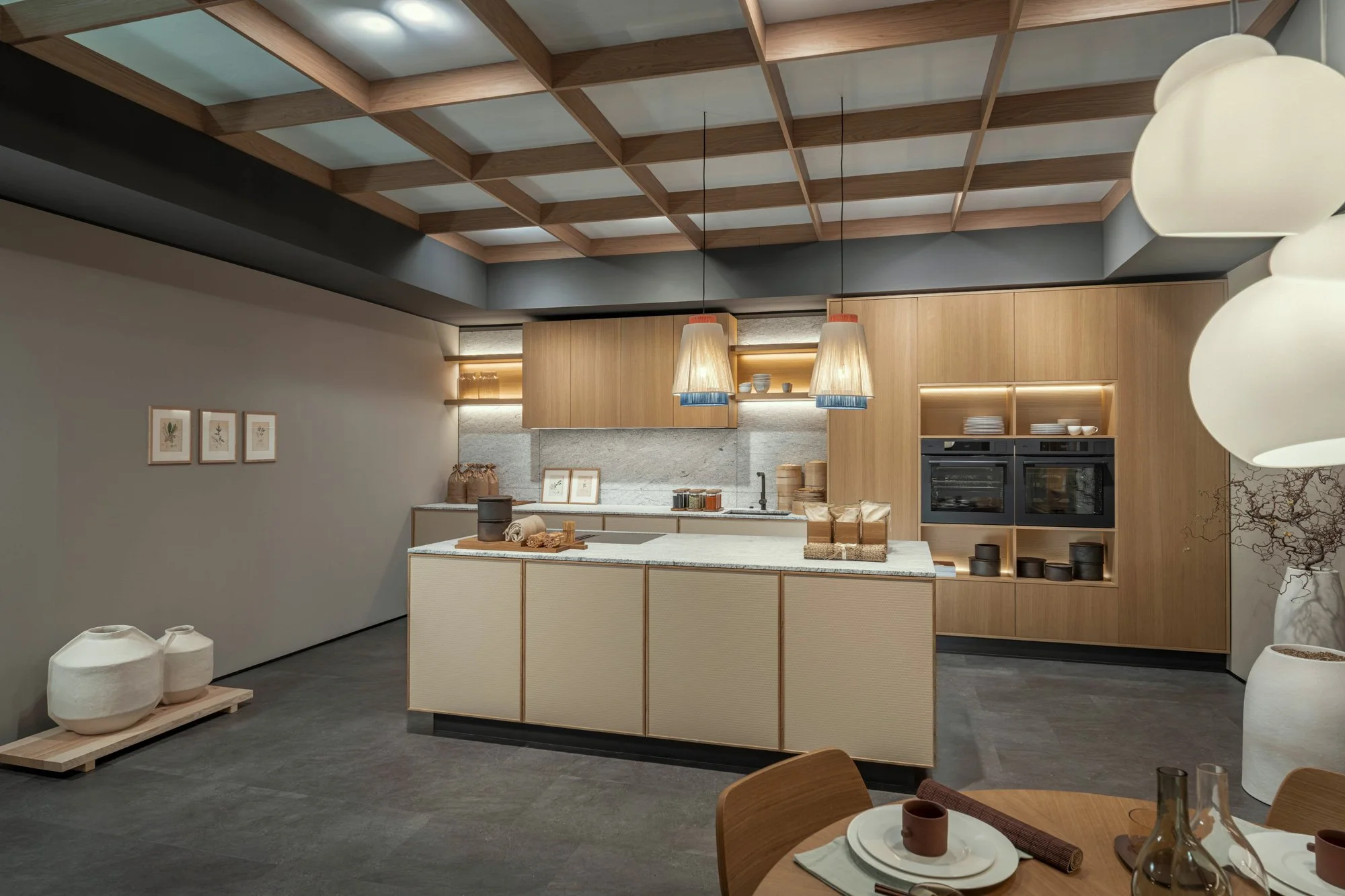 Une cuisine moderne avec un plafond en bois, éclairée par deux suspensions, avec des étagères éclairées en bois contenant de la vaisselle, un plan de travail en pierre avec des ustensiles et des décorations, et un espace à manger avec des chaussettes