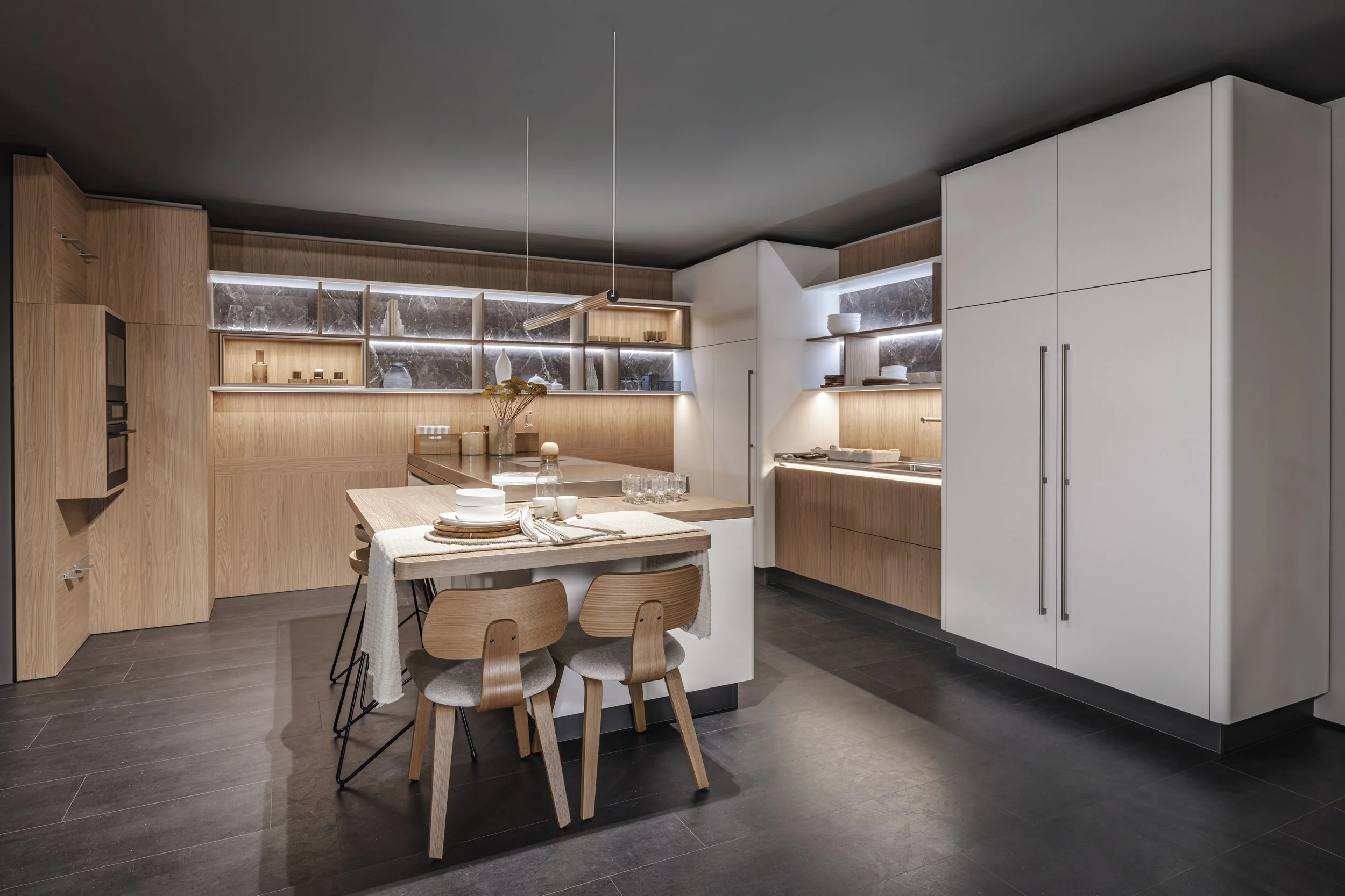 Cuisine moderne avec bois clair, blanc et marbre, table en bois avec vaisselle et chaises en bois, étagères décoratives illuminées.