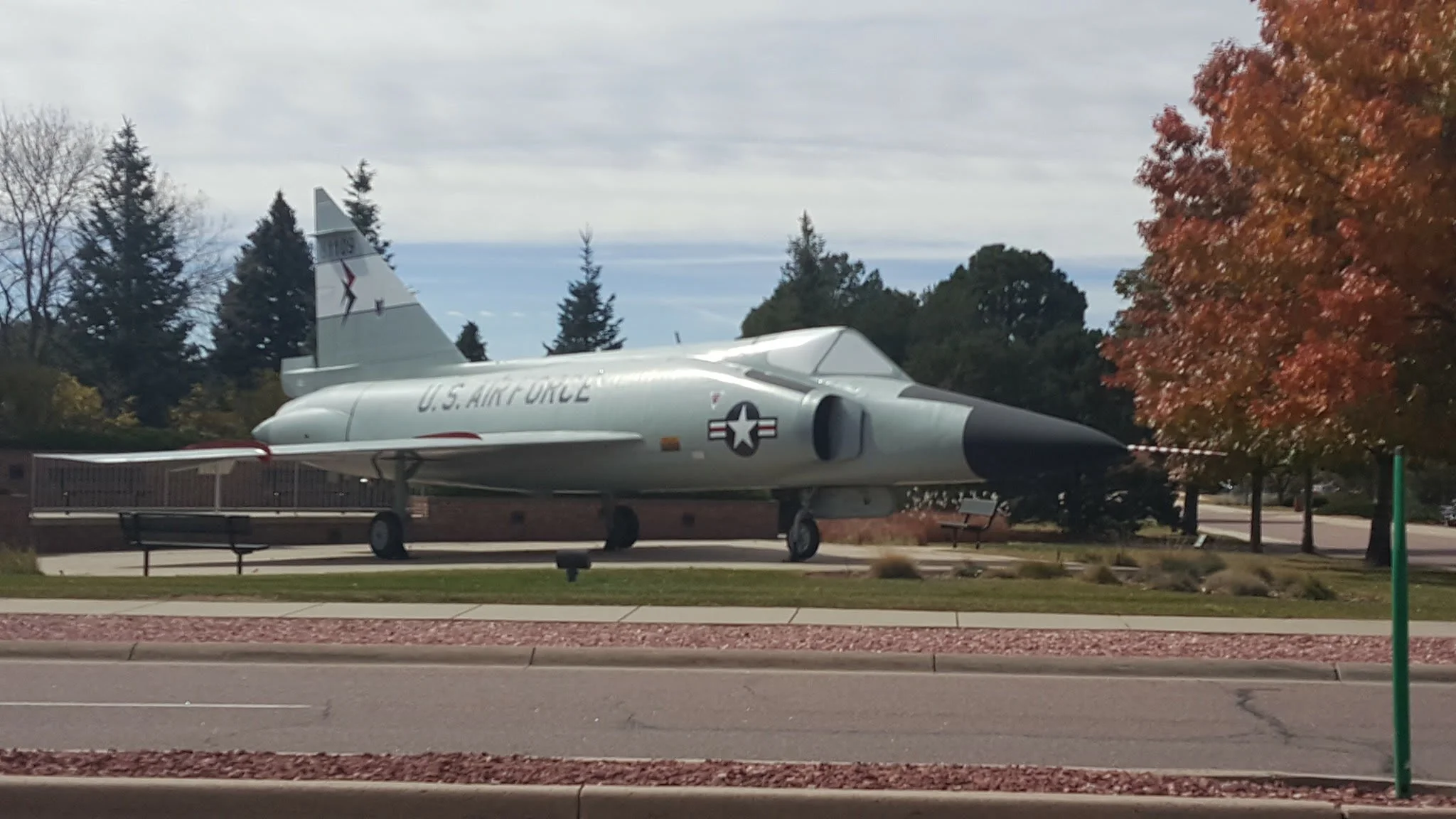 A decommissioned U.S. Air Force Phantom fighter jet displayed outdoors in a park with trees showing fall foliage.