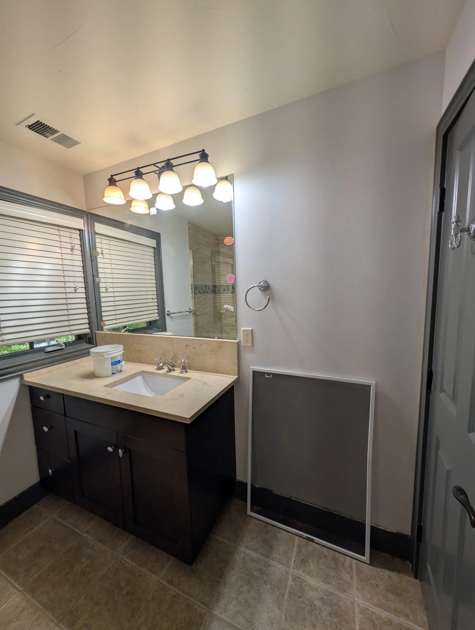 Bathroom mirror above a sink with a vanity, window with blinds, light fixture, and shower door.