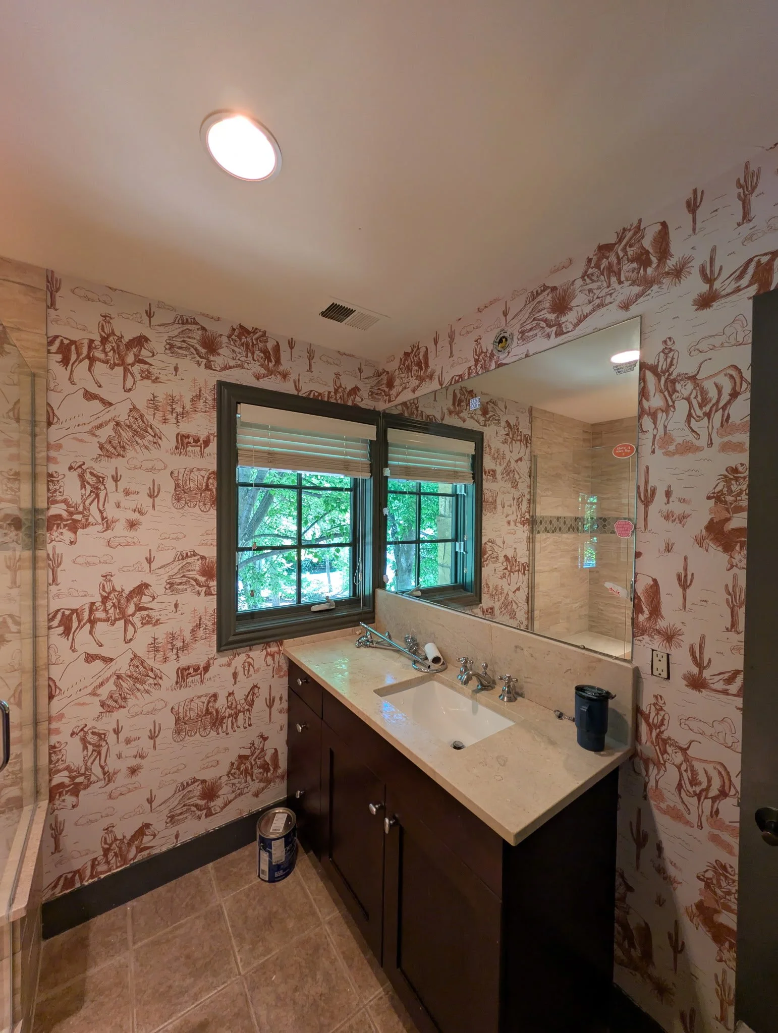 Bathroom with a single sink vanity, a large mirror, window with blinds, and western-themed wall decor featuring cowboys, horses, cacti, and desert scenery.
