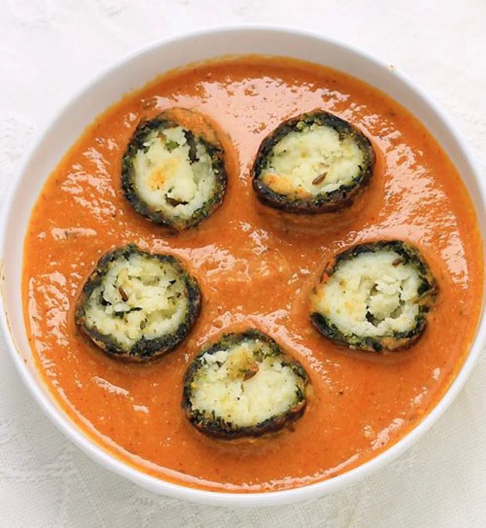 A bowl of spicy tomato-based Indian curry with five pieces of stuffed eggplant roll.