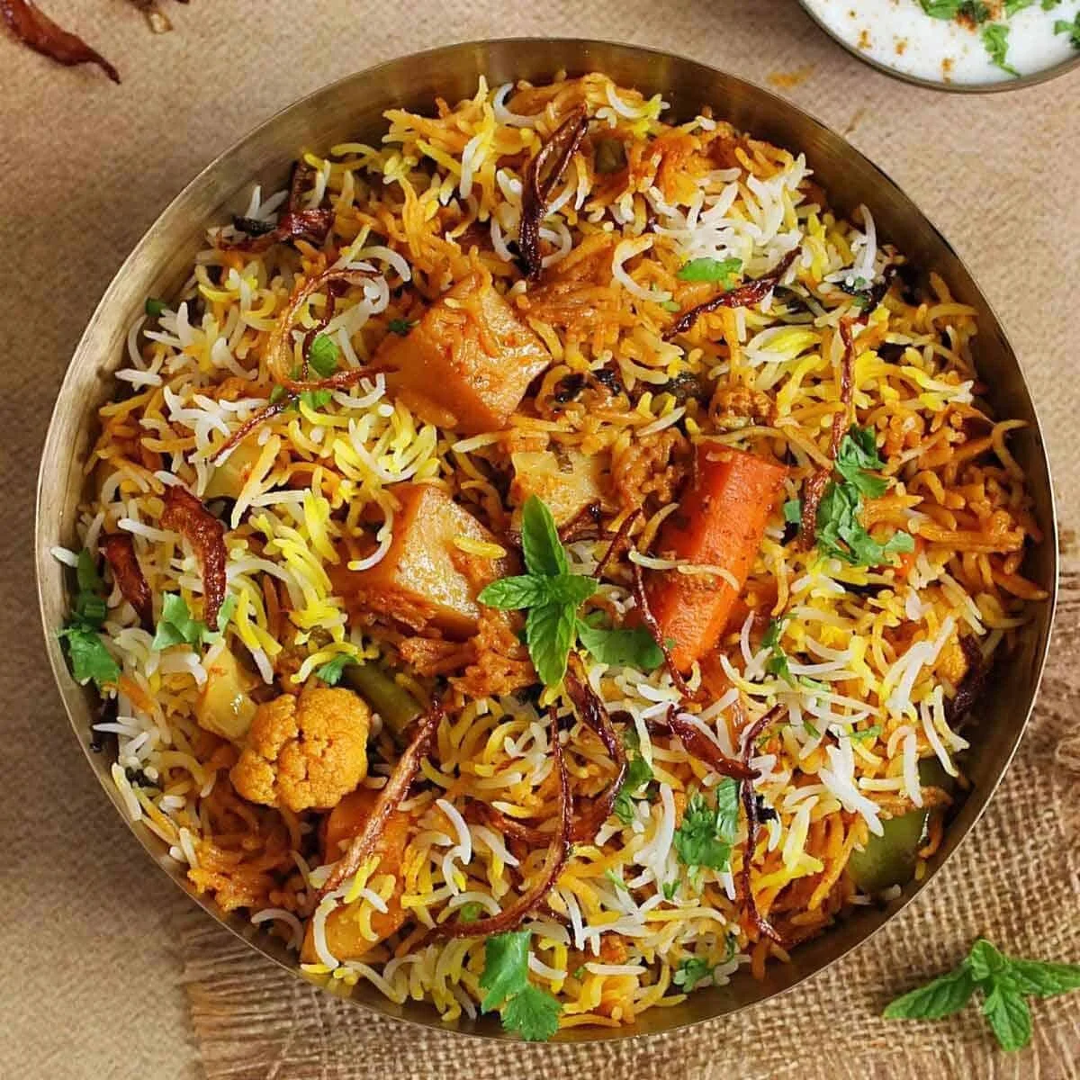 A bowl of Indian vegetable biryani with rice, carrots, cauliflower, and spices garnished with fresh herbs.